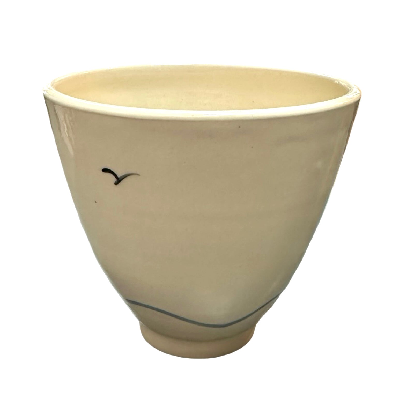 The back of a cream ceramic beaker with a black seagull flying and a blue wave along the base.