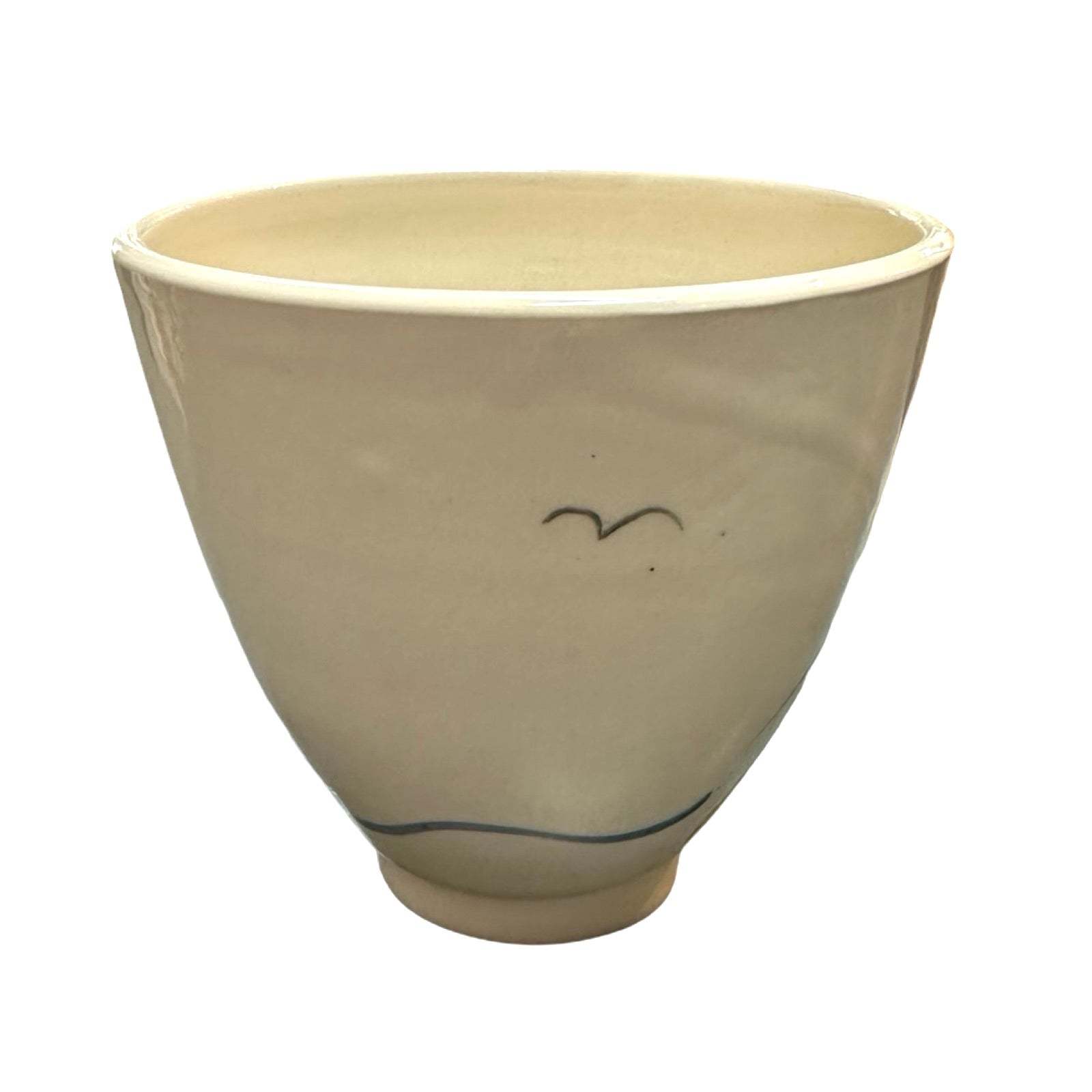 The back of a cream ceramic beaker with a black seagull flying and a blue wave along the base.