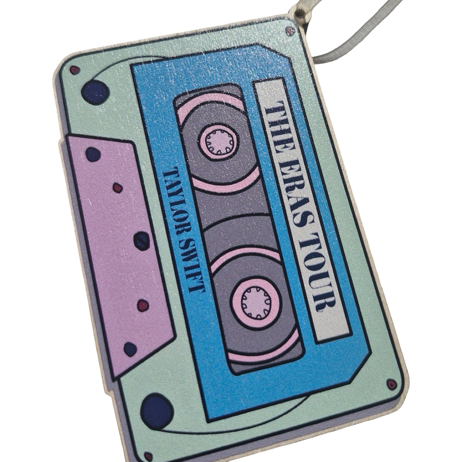 A rectangular-shaped wooden decoration featuring an illustration of a retro cassette tape in blue, pink and aqua with the title 'The Eras Tour, Taylor Swift'.