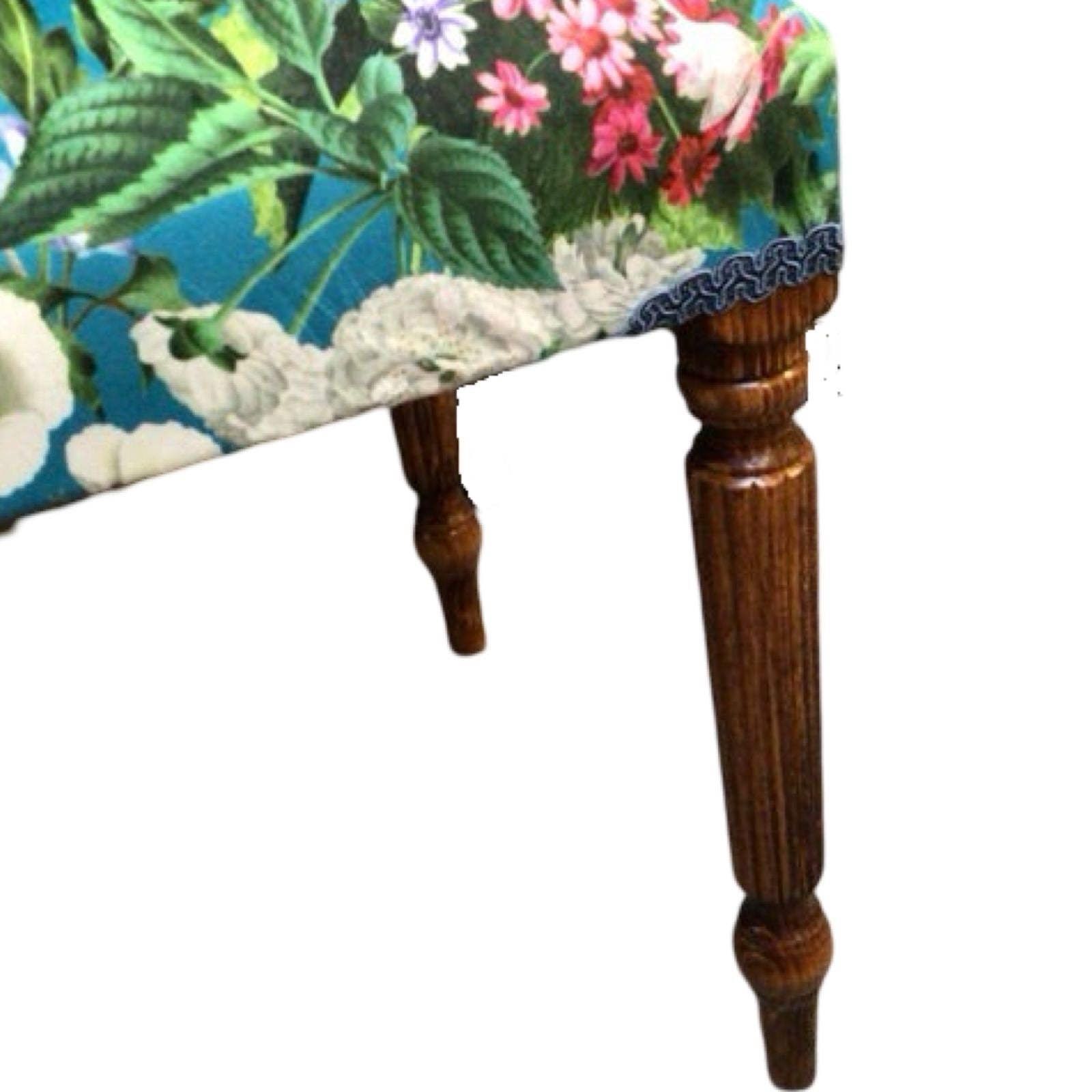 A rectangular bench with mahogany legs and a luxurious velvet fabric upholstery featuring a bright colourful floral design.