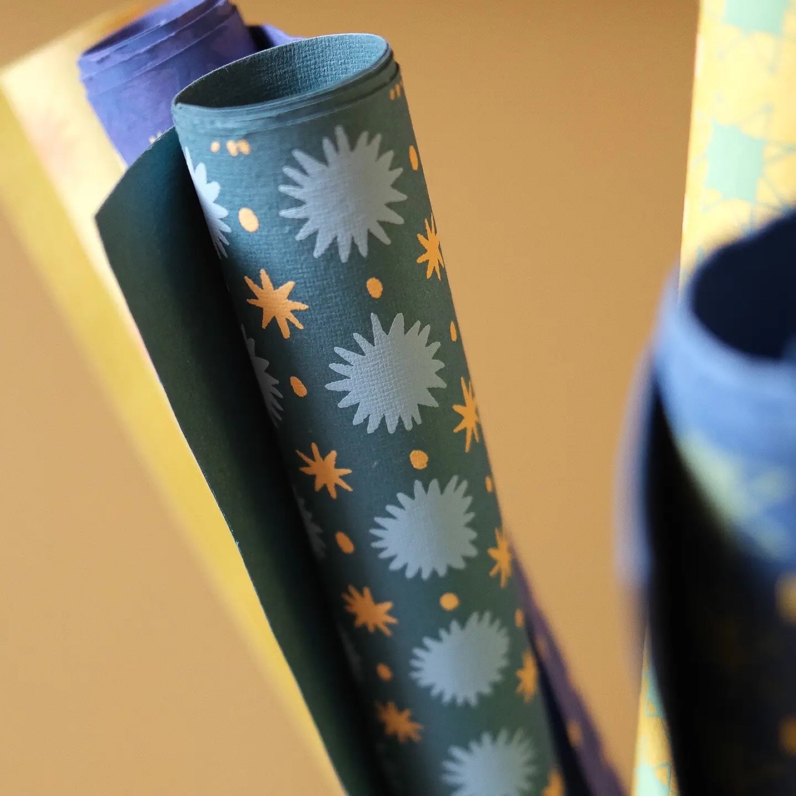 A roll of screen-printed wrapping paper with turquoise and yellow stars against a teal background.