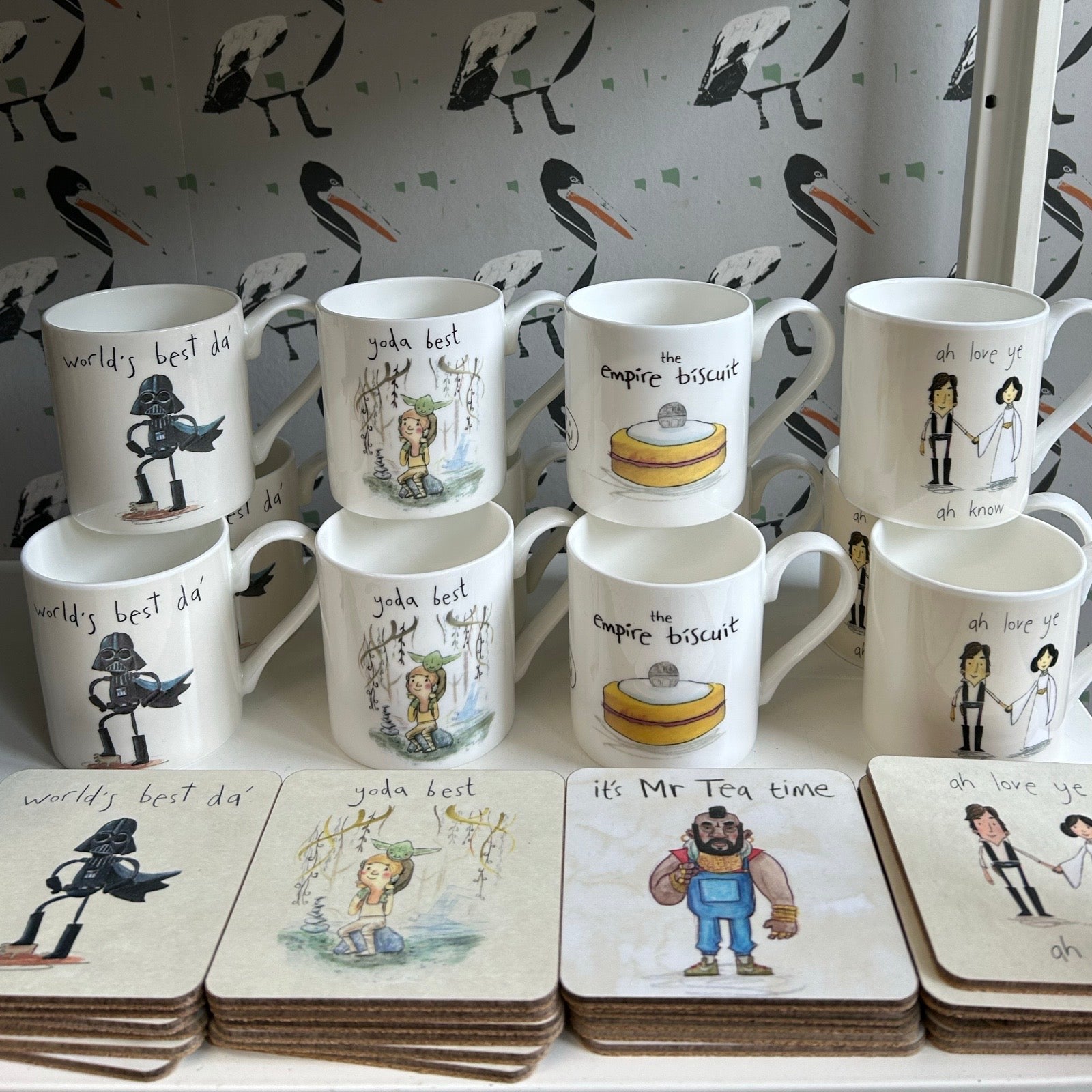 Collection of mugs and coasters with various designs on a white surface.