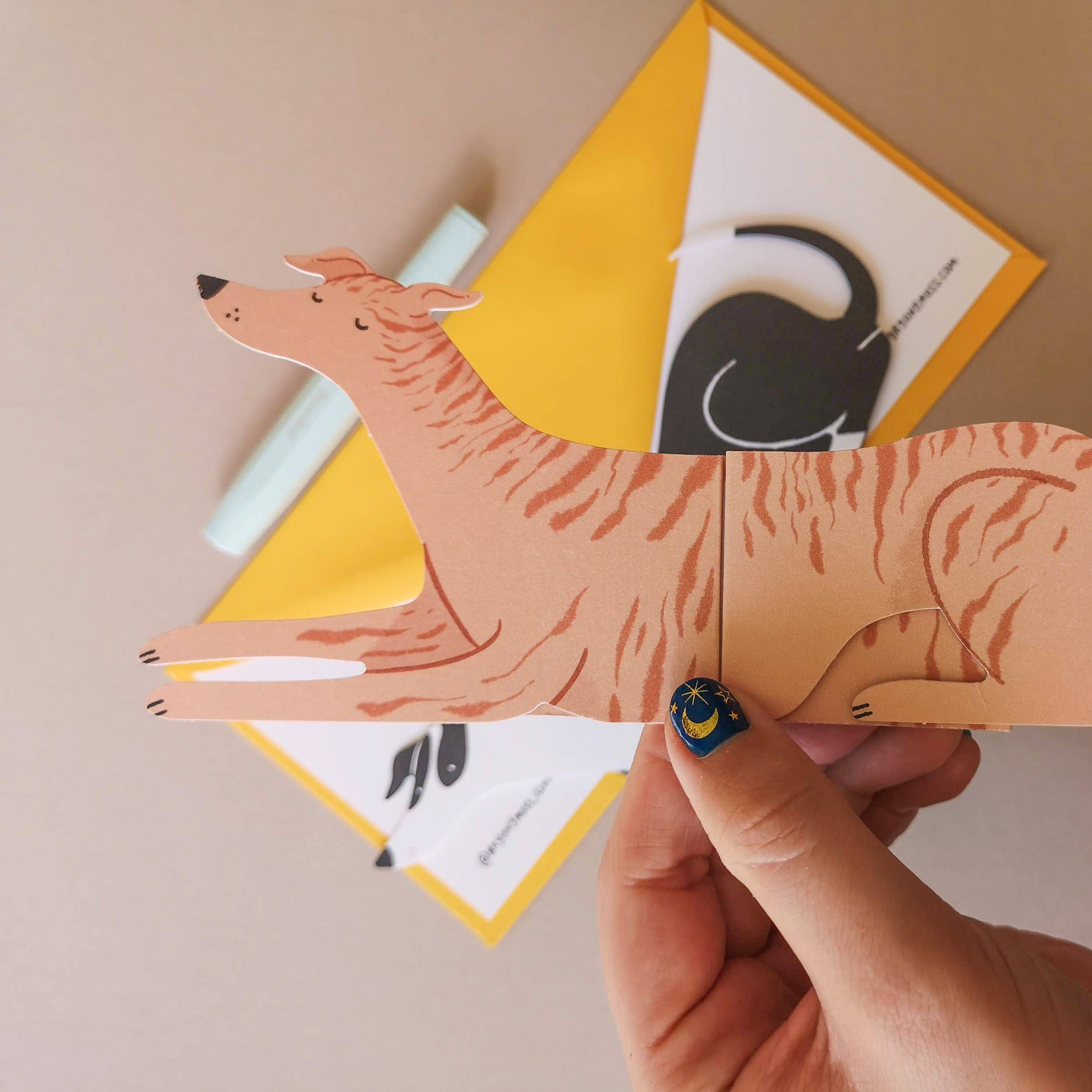 Hand holding a paper dog card with an envelope in the background.