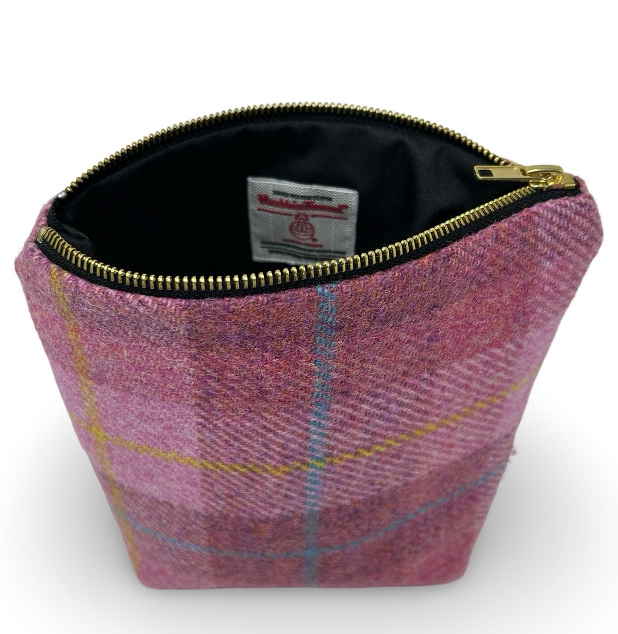 Pink Harris tweed toiletry bag shown here with the gold zip open.  The waterproof black lining has a Harris tweed orb label sewn onto it.