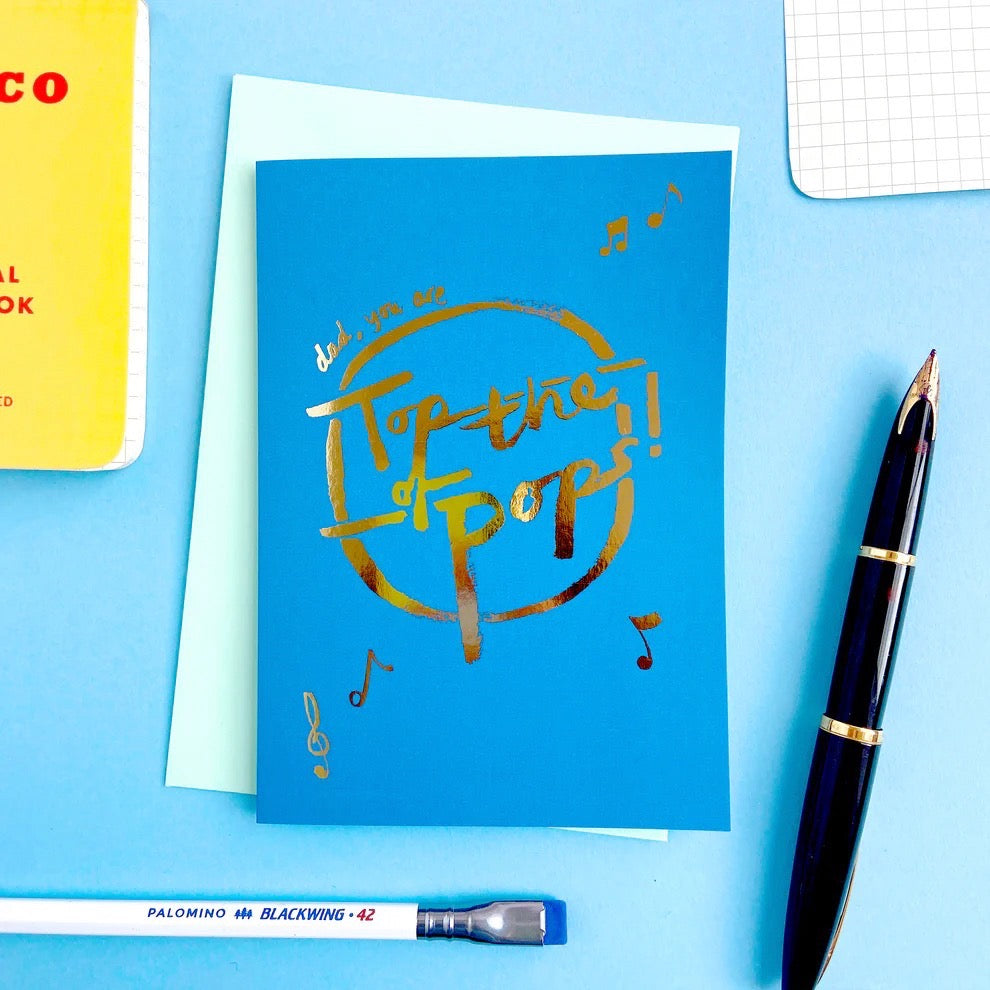 Blue card with gold text 'Top of the Pops!' on a blue background with stationery items.