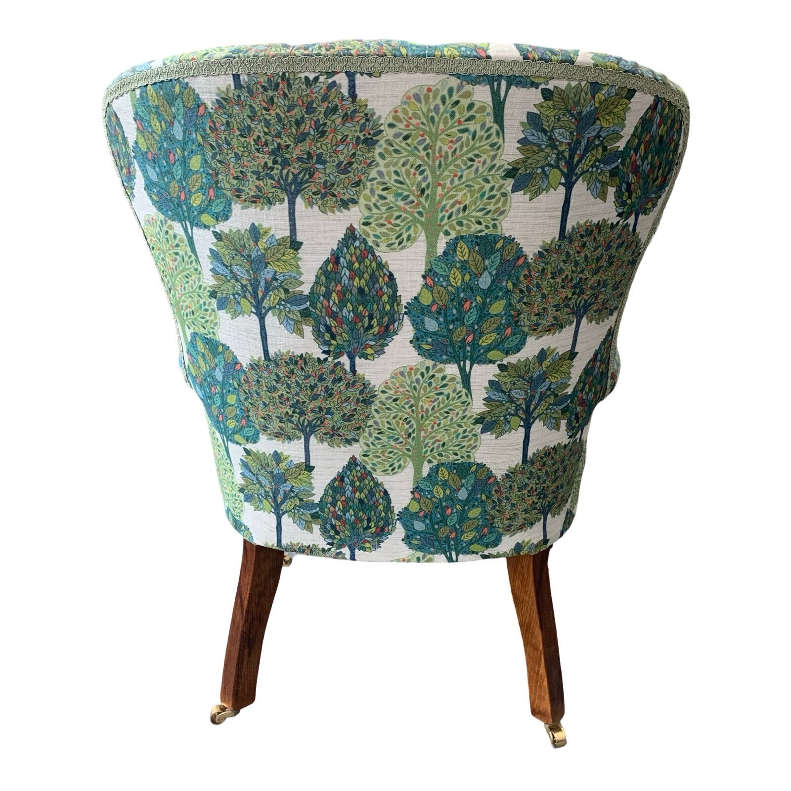 A cream linen armchair with a blue and green tree pattern, featuring a button-back design, mahogany legs, and gold castors.
