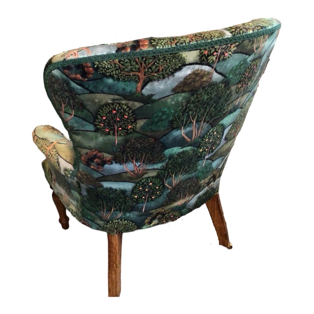 A green velvet armchair with a pattern of trees and hills, featuring a button-back design and mahogany legs.