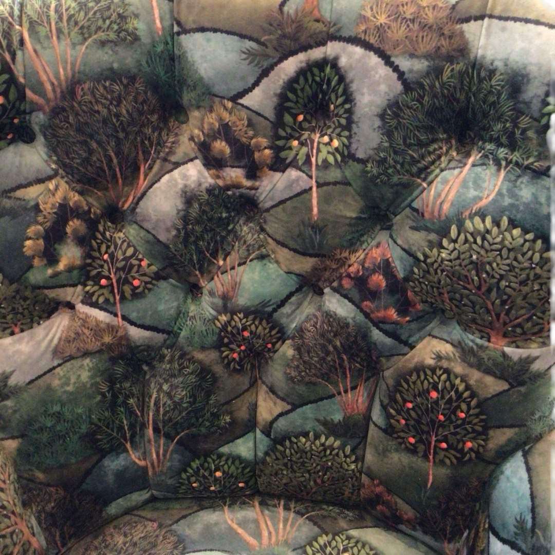 A green velvet armchair with a pattern of trees and hills, featuring a button-back design and mahogany legs.