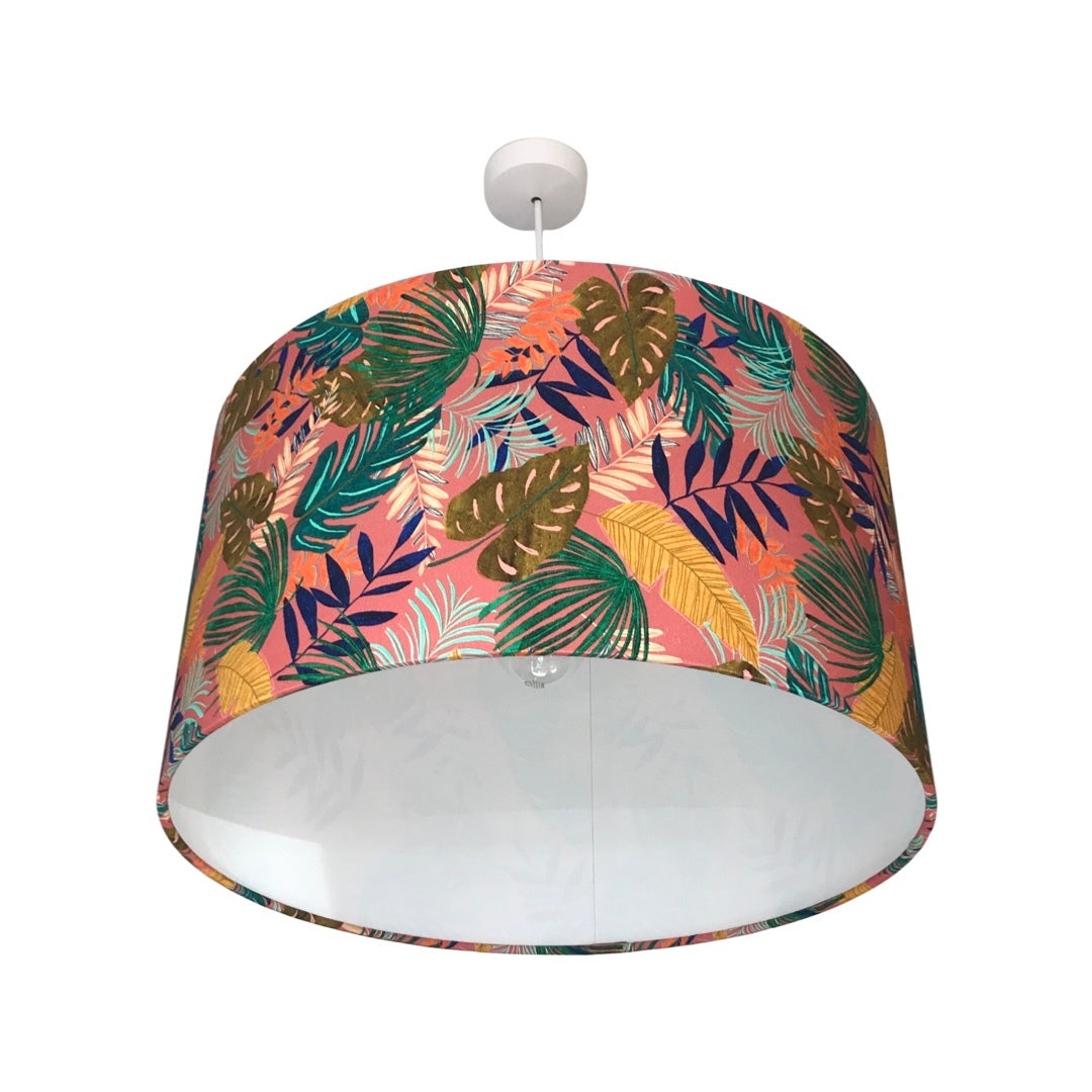 Drum lampshade covered in tropical leaves in shades of green, blue and yellow on a pink background