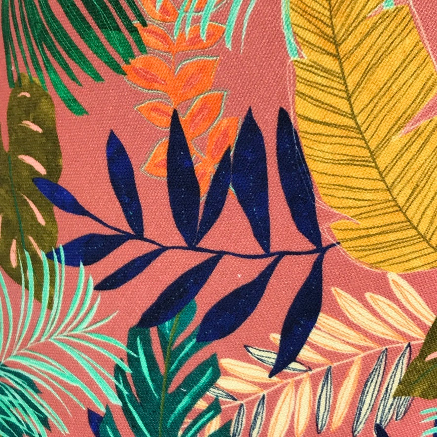 Fabric covered in tropical leaves in shades of green, blue and yellow on a pink background