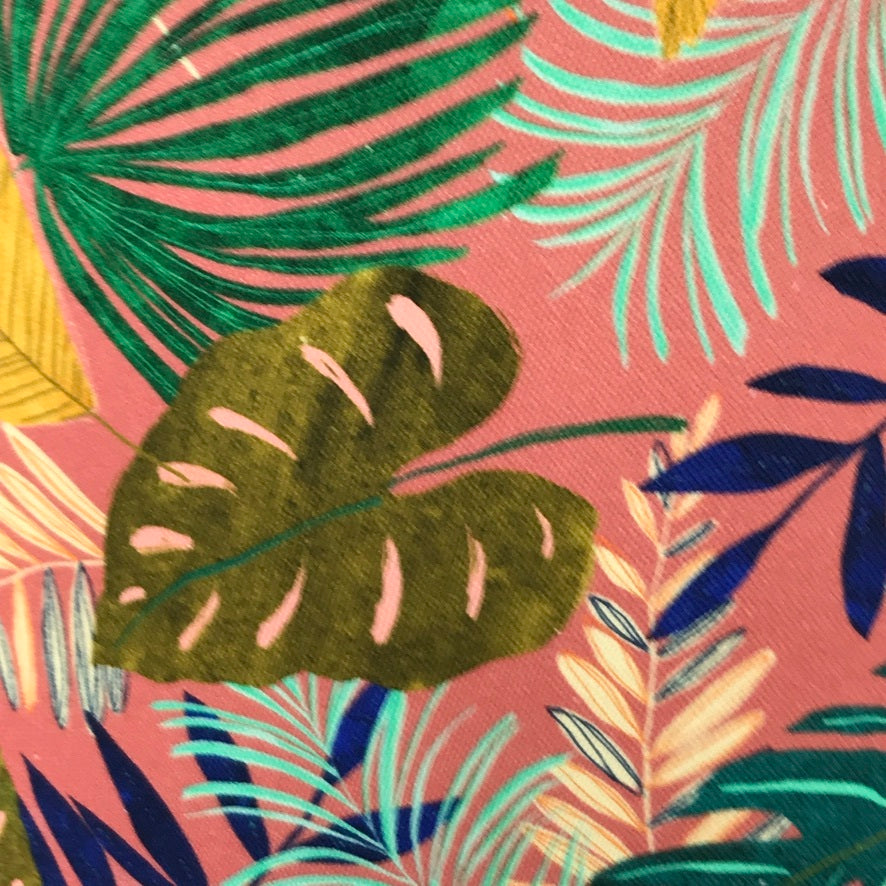 Fabric covered in tropical leaves in shades of green, blue and yellow on a pink background