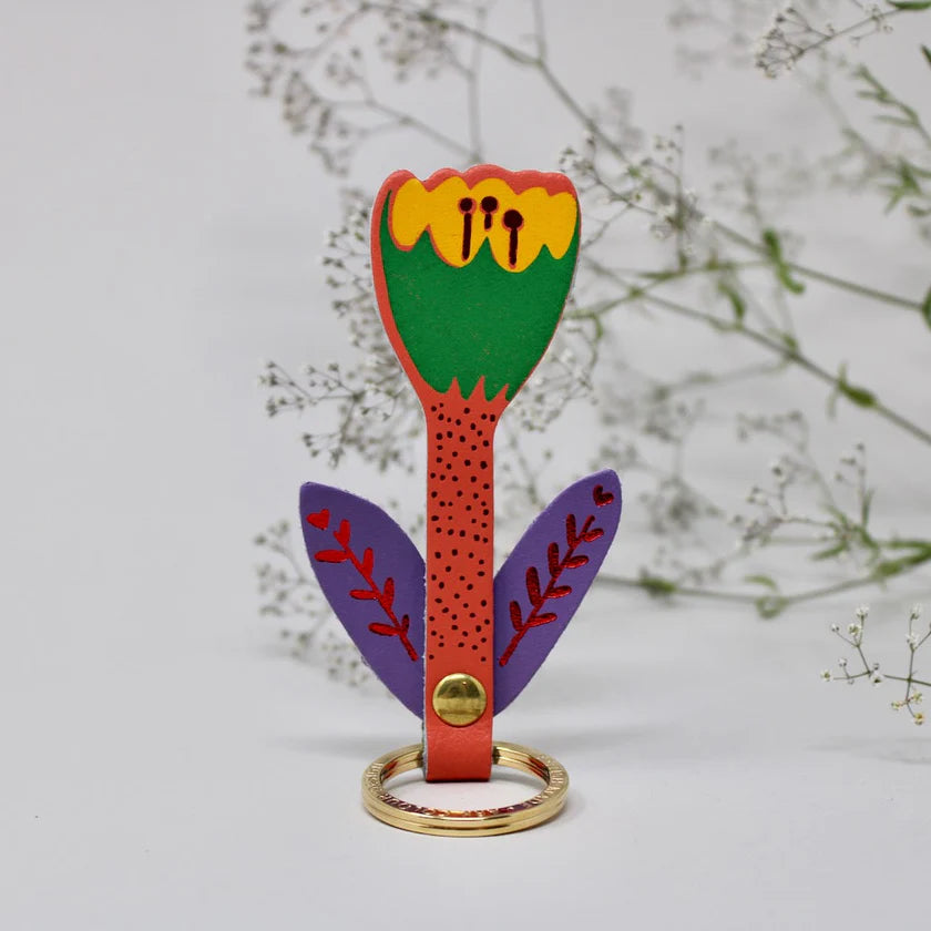 Colourful key ring shaped like a flower with a gold ring on a light grey background.