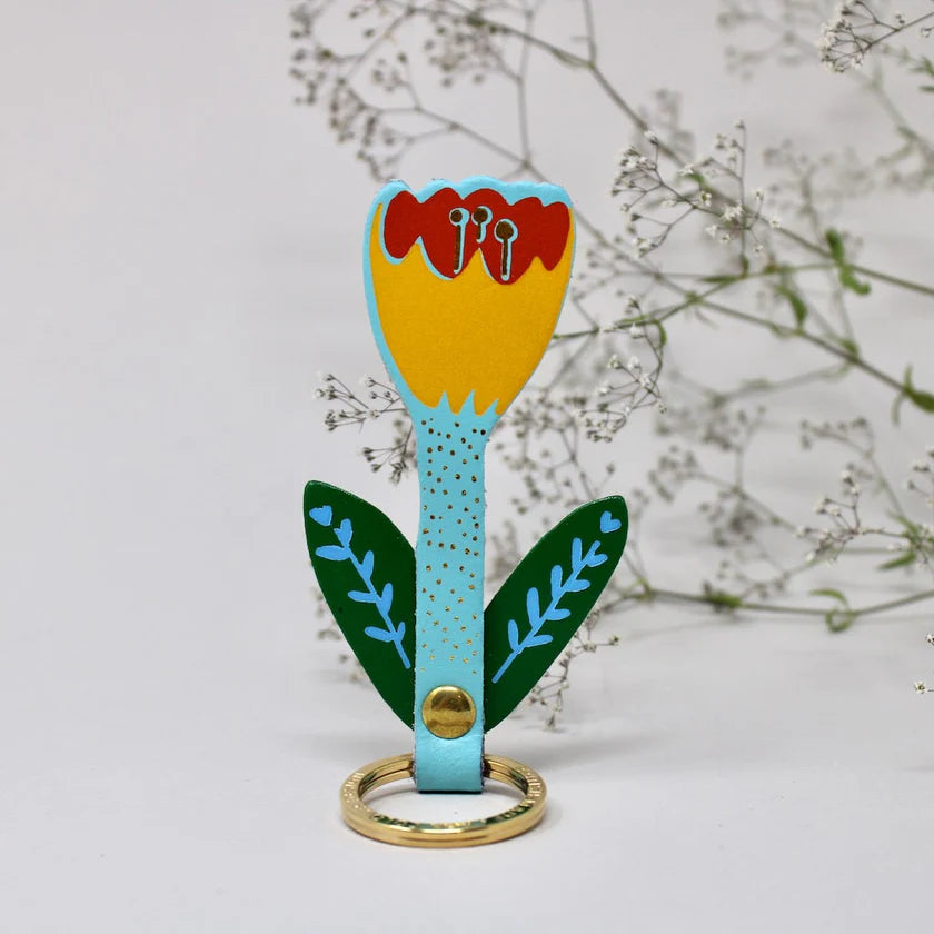 Decorative key ring shaped like a flower with a gold ring on a light grey background.