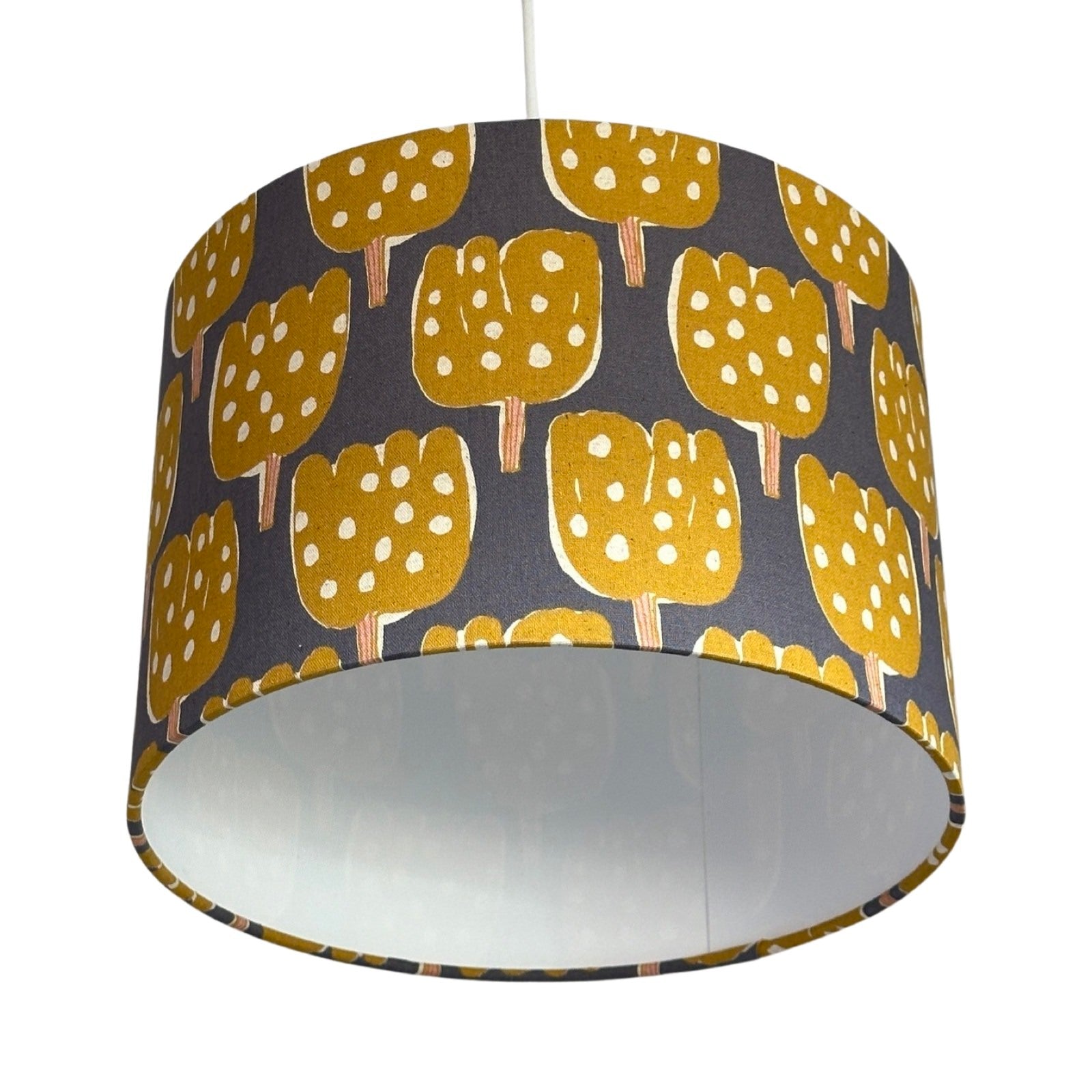 Close up of a drum lampshade covered in grey canvas fabric with mustard tulip-shaped trees with pale pink tree trunks
