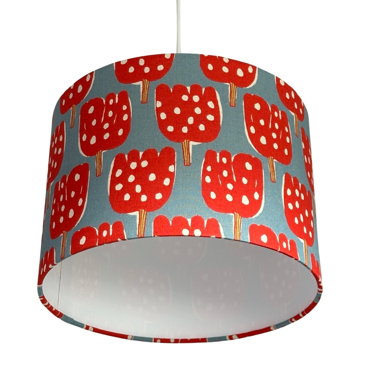 Close up of a drum lampshade covered in pale blue canvas fabric with red tulip-shaped trees with red and lime green tree trunks