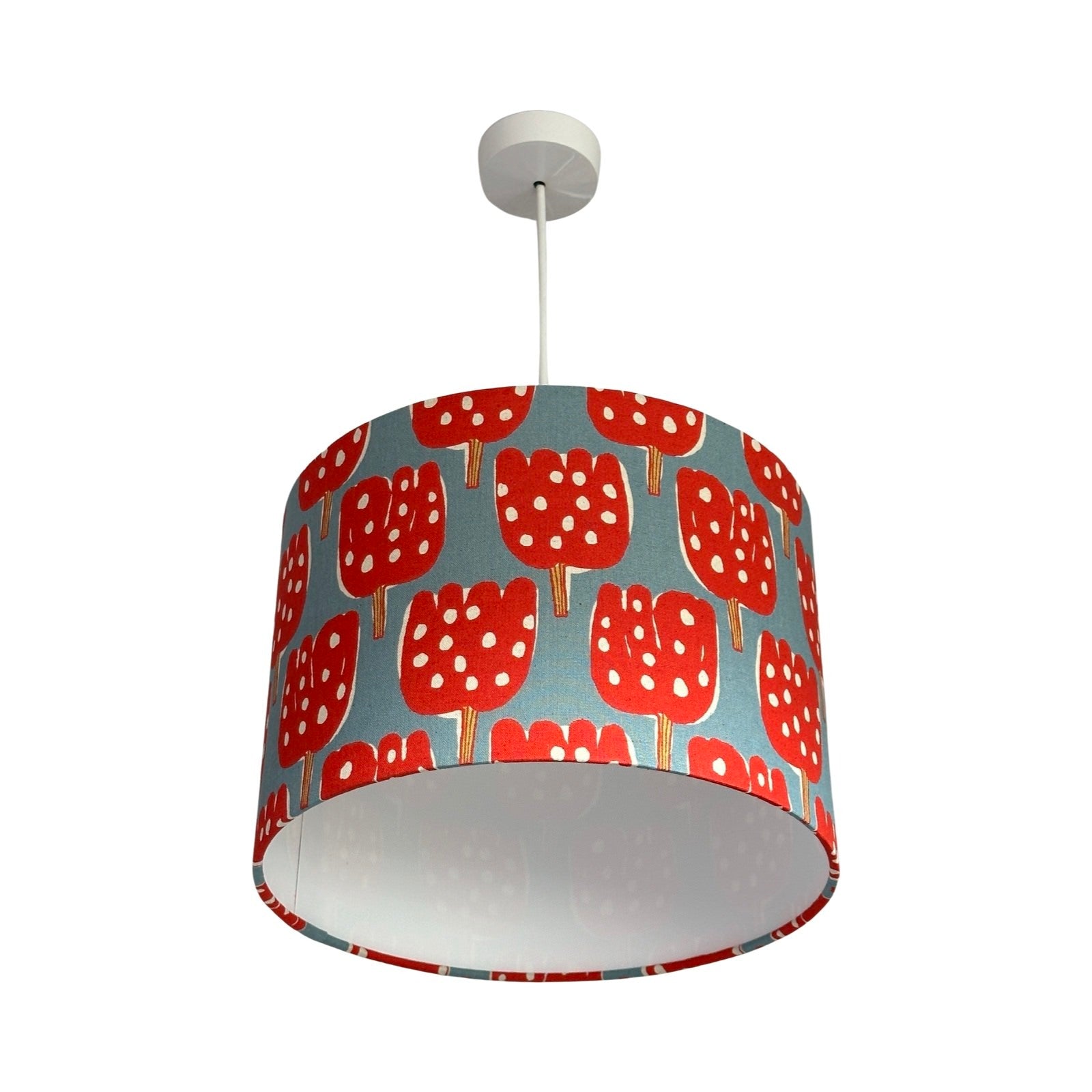 Drum lampshade covered in pale blue canvas fabric with red tulip-shaped trees with red and lime green tree trunks