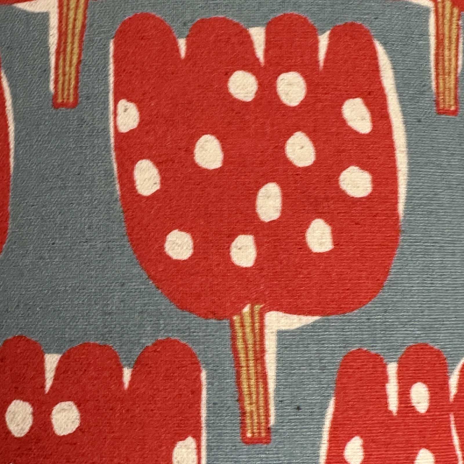 Close up of pale blue canvas fabric with red tulip-shaped trees with red and lime green tree trunks