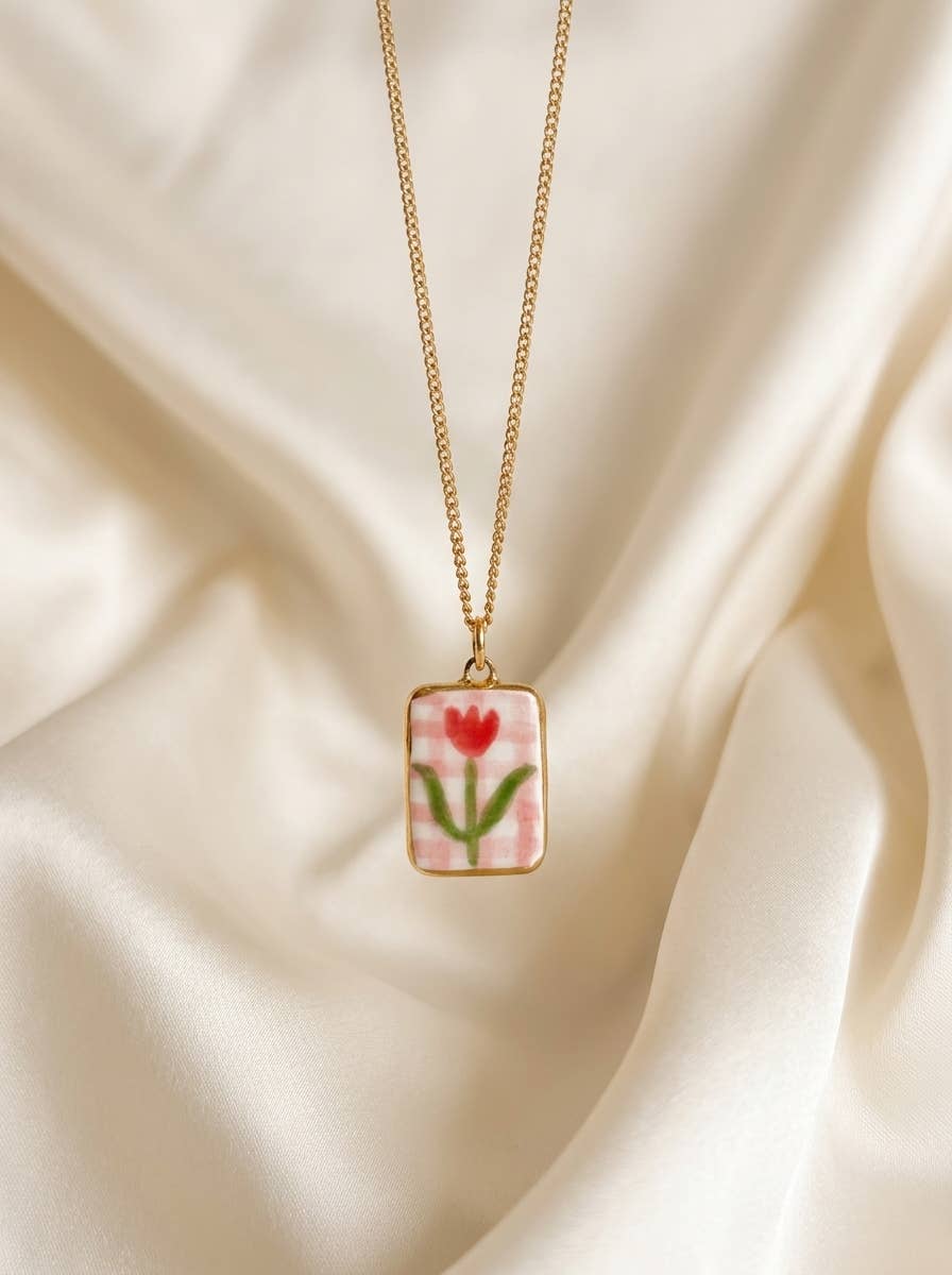 Necklace with a pendant featuring a red tulip and pink check background on a beige fabric background.