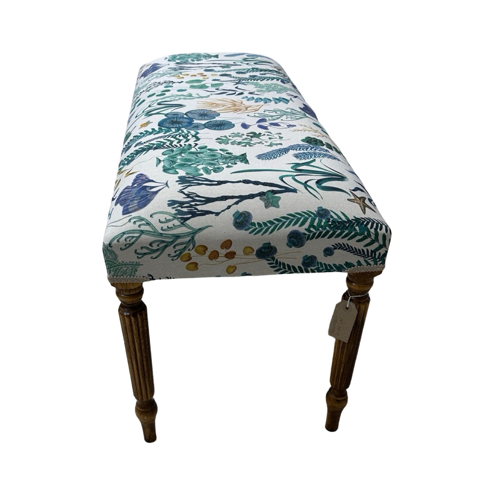 The end of a rectangular bench covered in a cream cotton/linen fabric with underwater designs in green, blue and mustard, cream binding and mahogany stained legs.