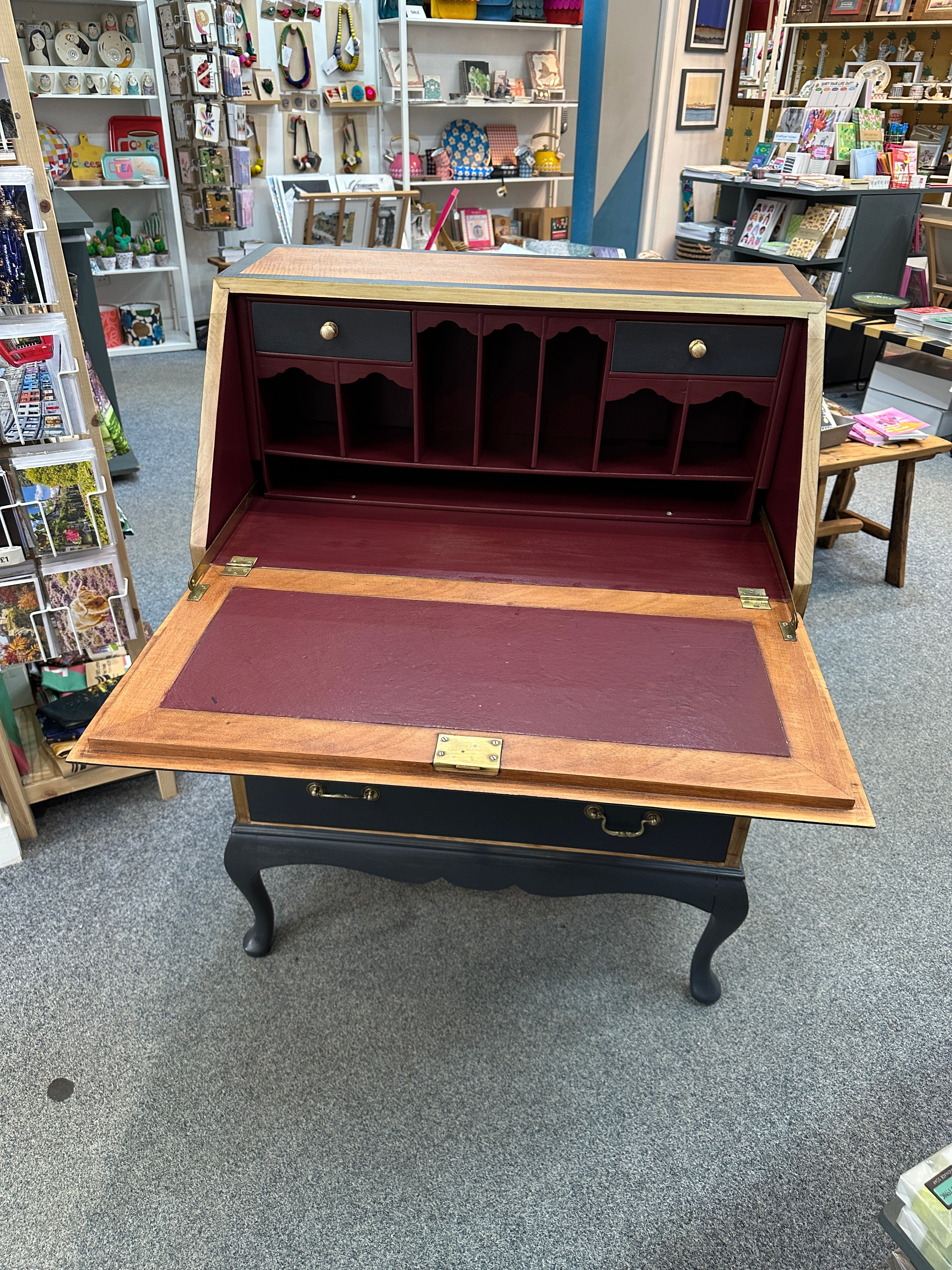 Wooden bureau with open lid on a gray floor.
