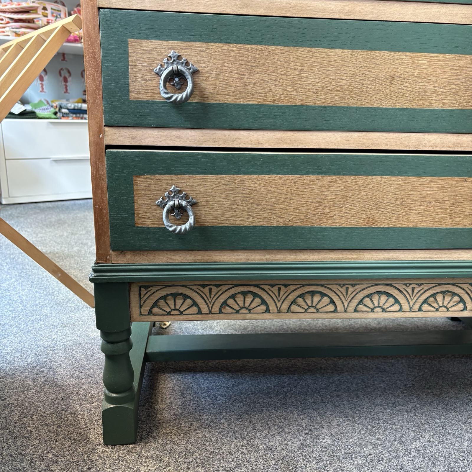 Wooden dresser with green base and decorative carvings on a carpeted floor.