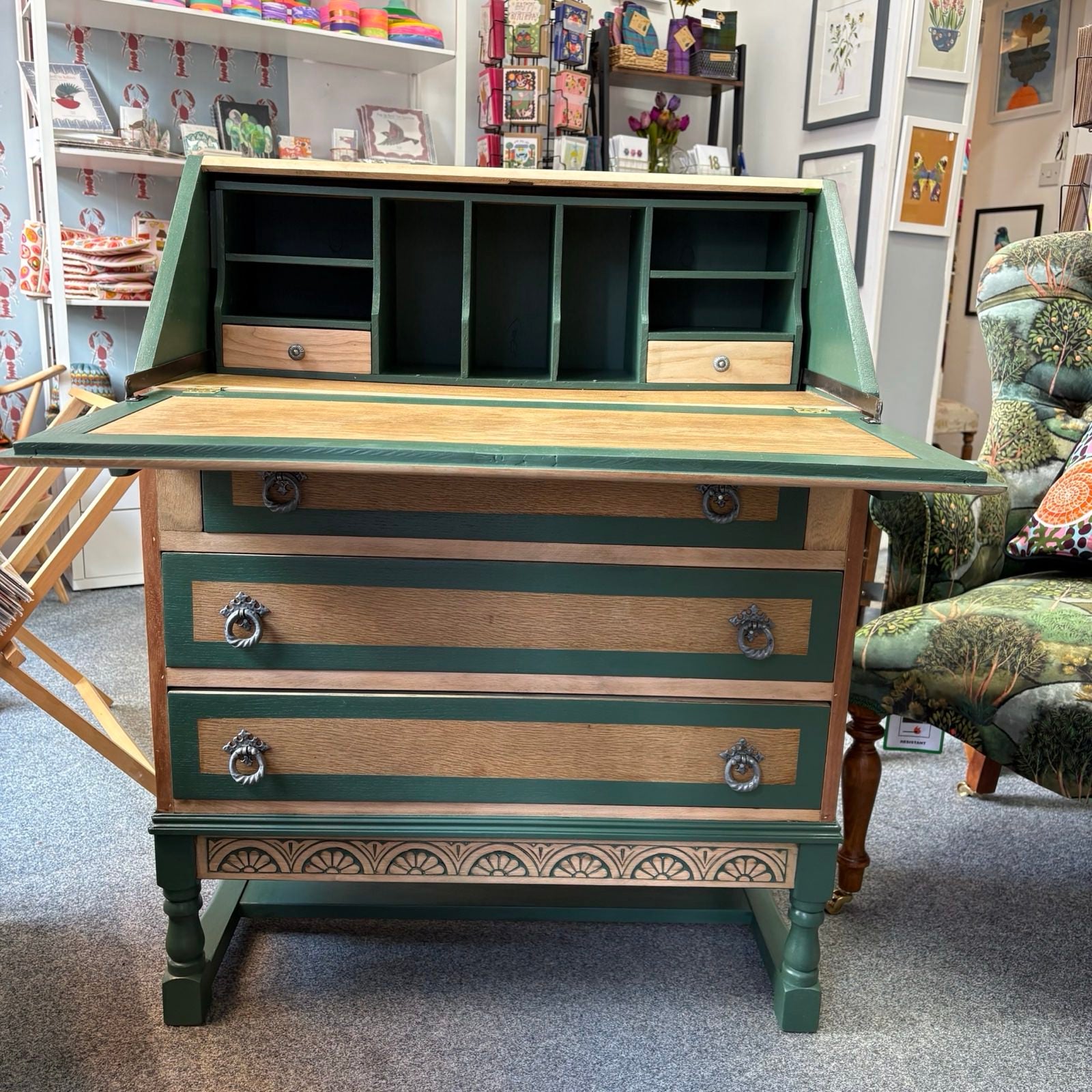Wooden desk with green accents in a room with shelves and decor.