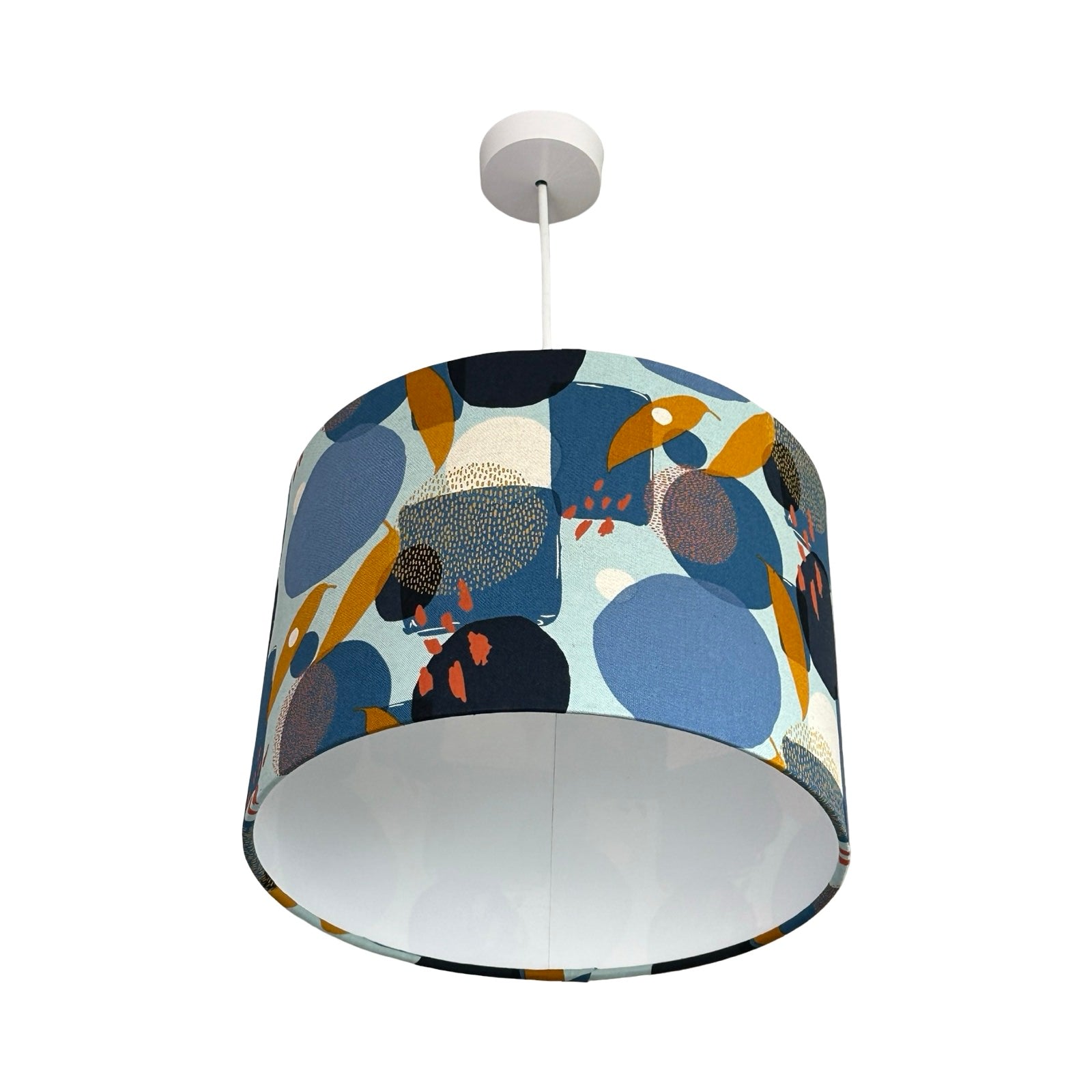 This drum lampshade is covered in light blue cotton fabric with a navy, blue, white and gold geometric pattern and a white inner lining.