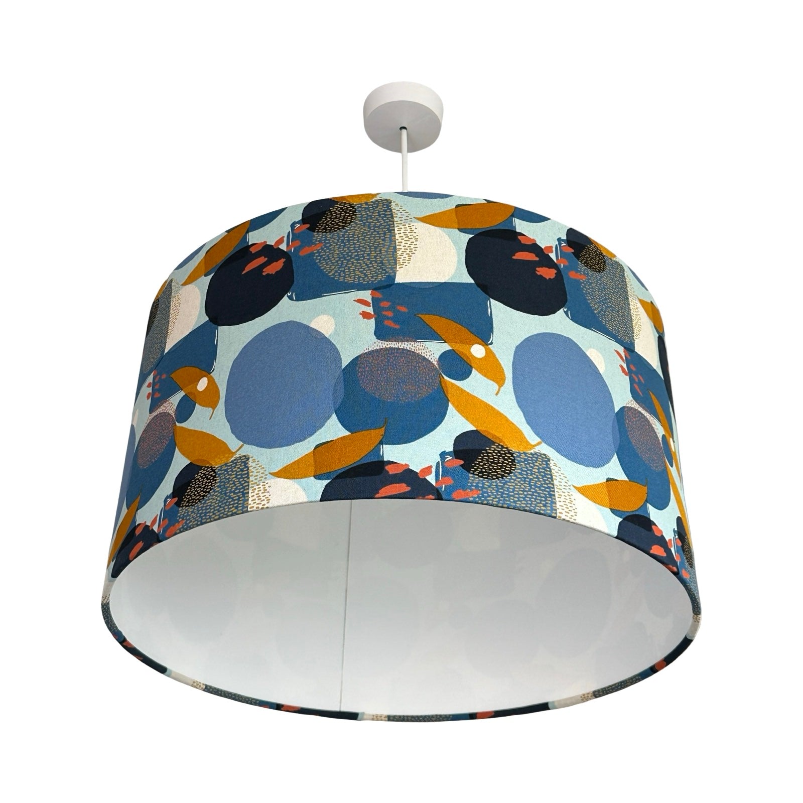 This drum lampshade is covered in light blue cotton fabric with a navy, blue, white and gold geometric pattern and a white inner lining.