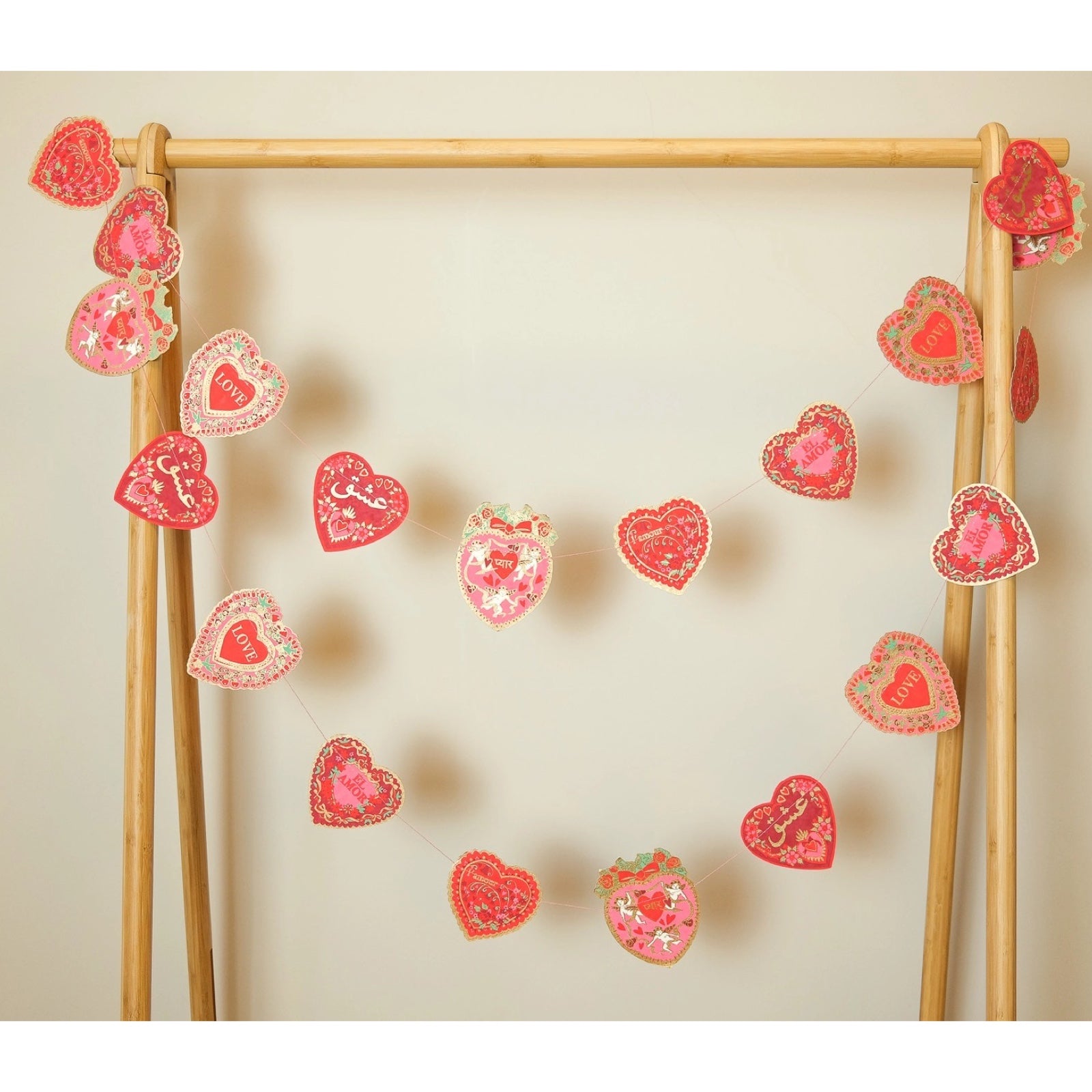 A Valentine's paper garland featuring twenty screen-printed love hearts in reds, pinks and gold. Each heart features the word 'love' in a different language hanging from a wooden frame.