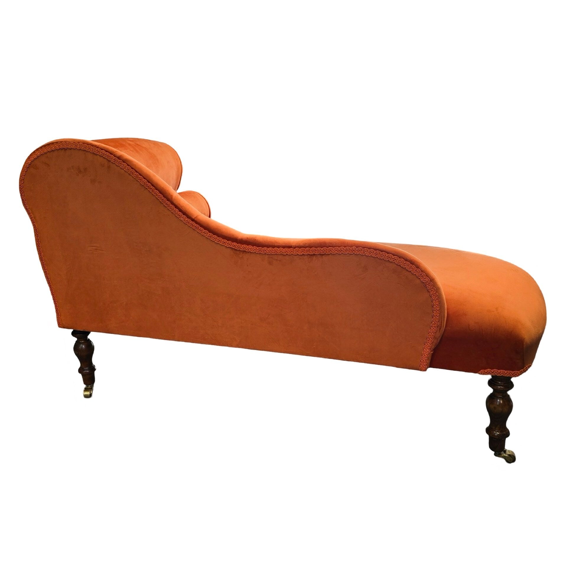 An orange velvet chaise longue with mahogany stained legs and brass coloured castors.