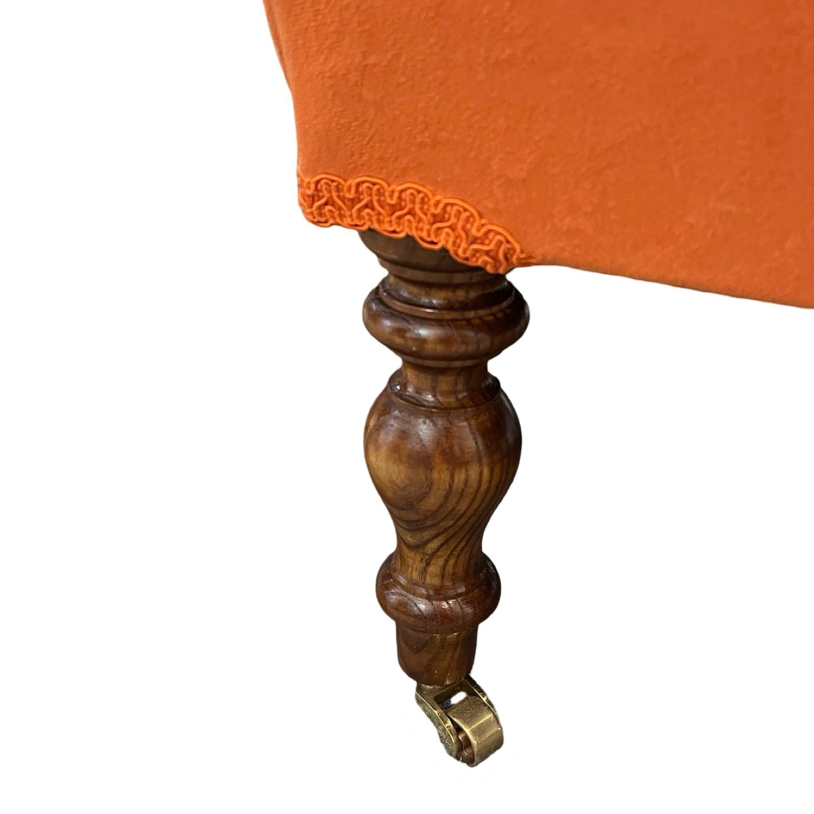 An orange velvet chaise longue with mahogany stained legs and brass coloured castors.