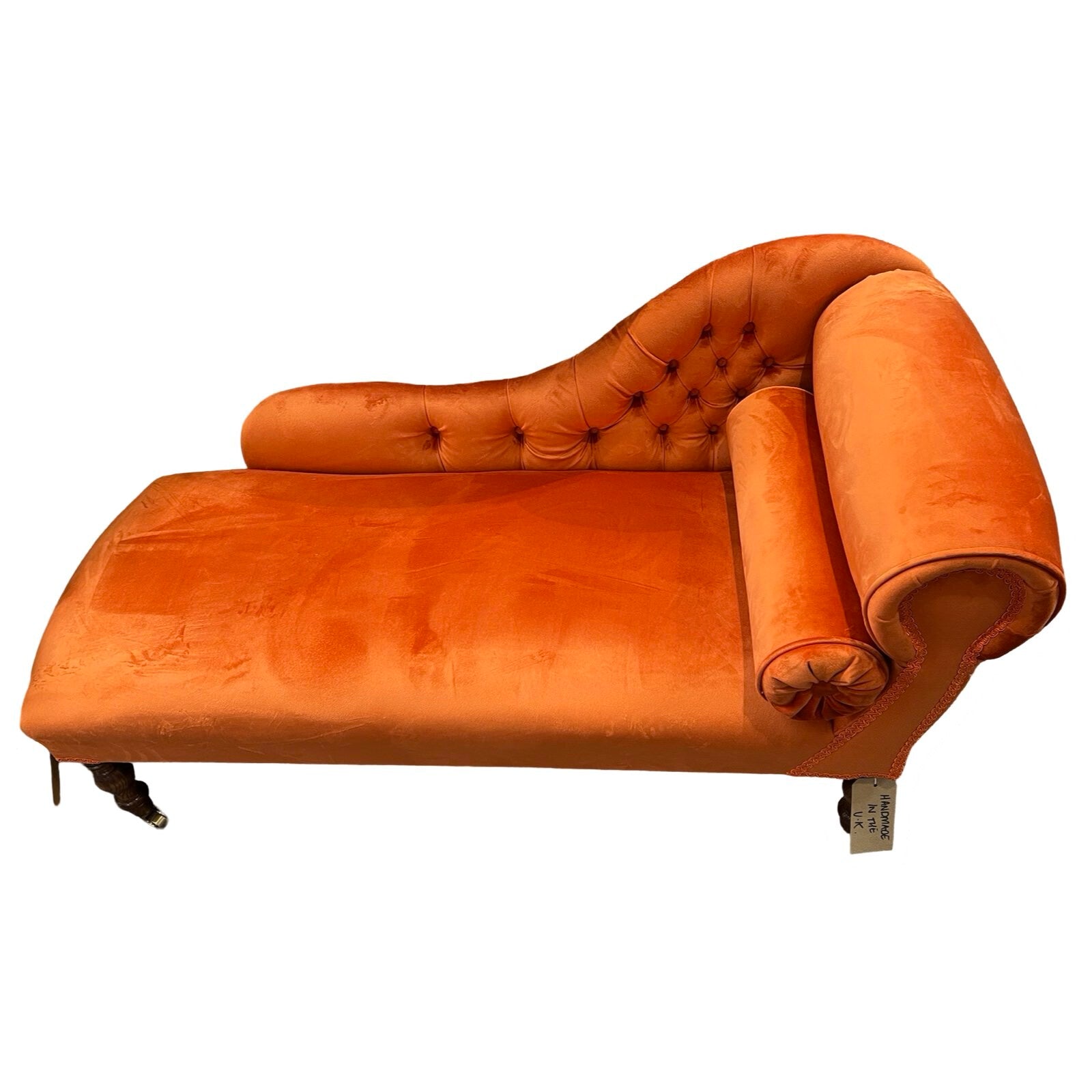 An orange velvet chaise longue with mahogany stained legs and brass coloured castors.