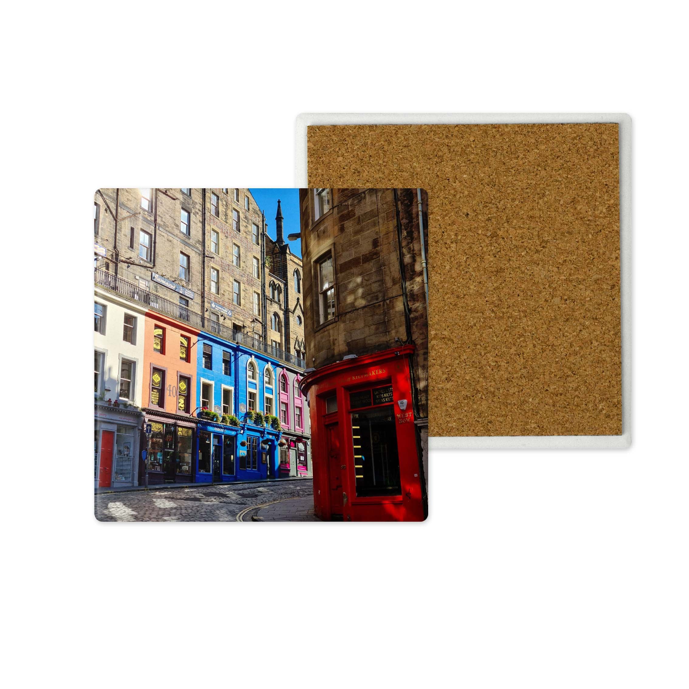 Two square cork coasters shown on a white background, one featuring a colourful street scene with buildings and a red building, and the other showing the plain cork backing.