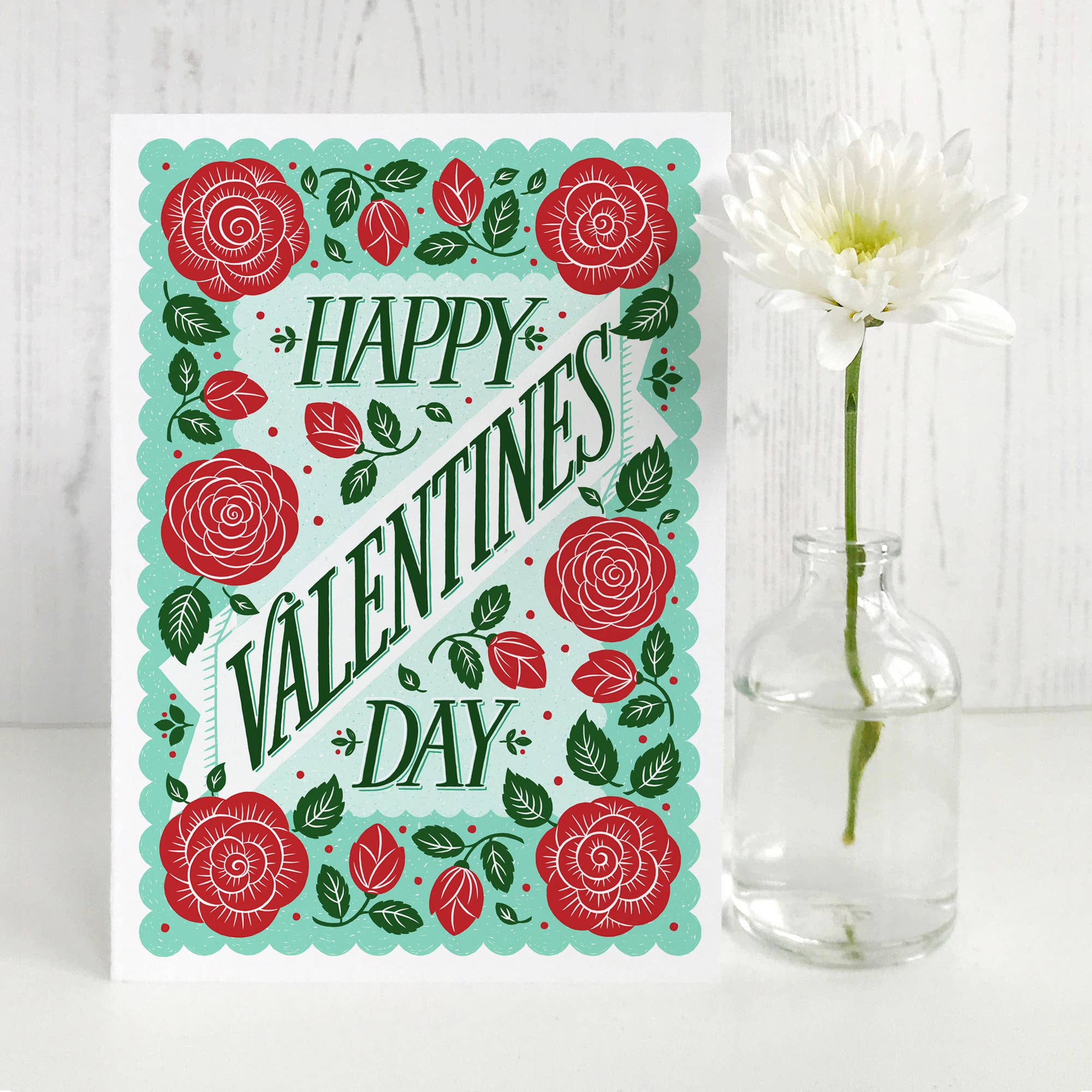 Valentine's Day card with red roses and green leaves on a white background with a flower.