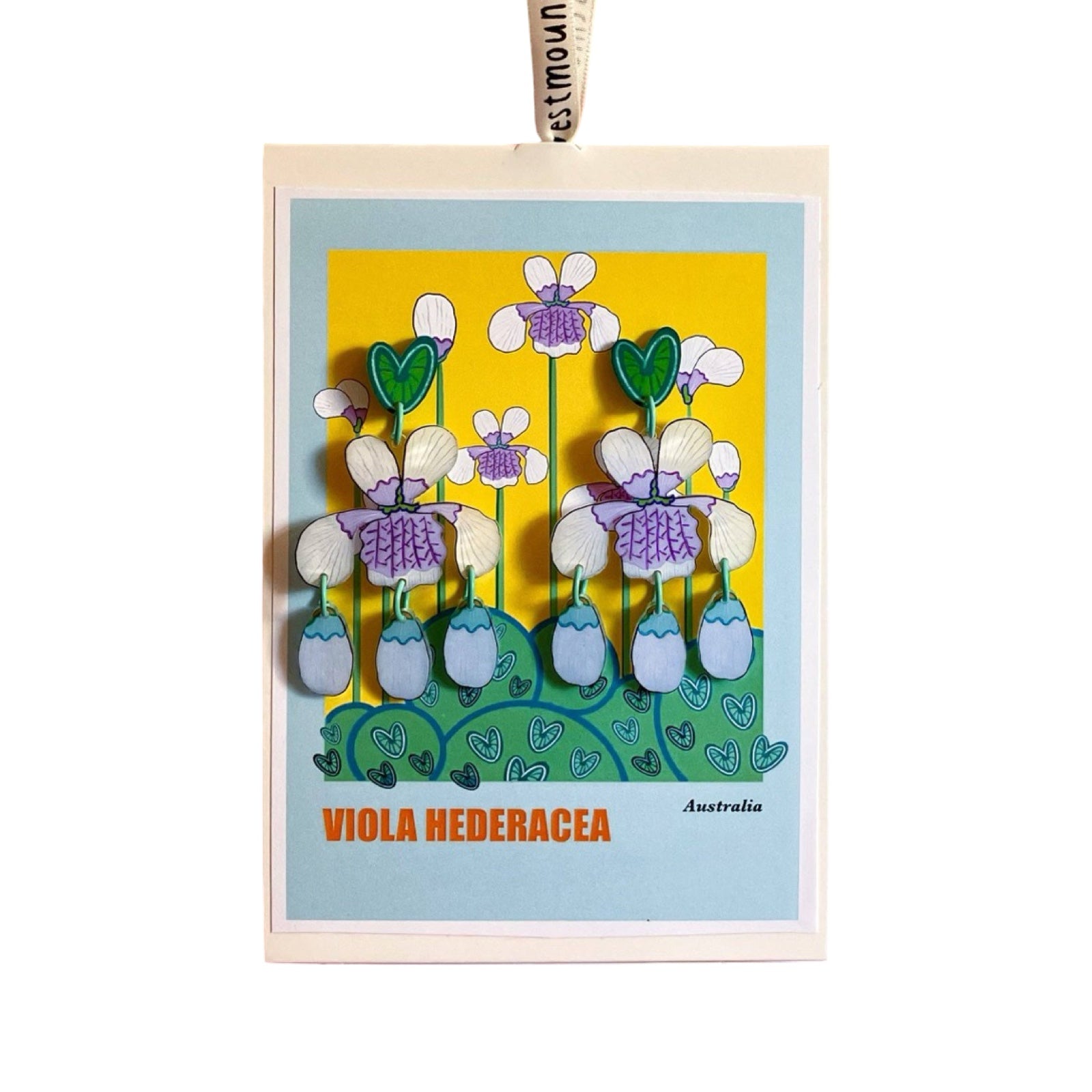 A pair of acrylic dangle earrings with green love heart studs, white and lilac viola flowers and lilac hanging petals, all on a matching backing card.