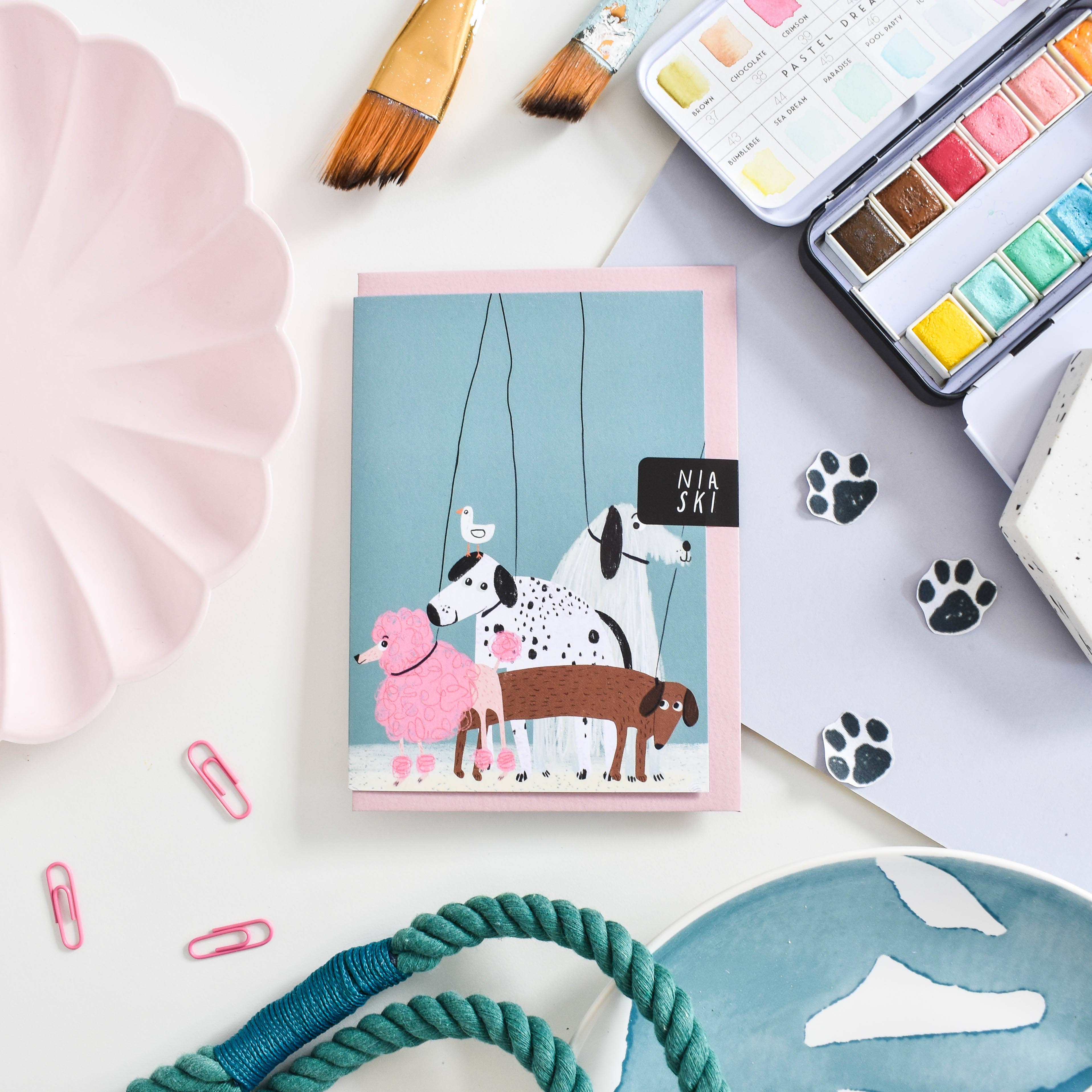 Card with dog illustration surrounded by art supplies on a light grey background.