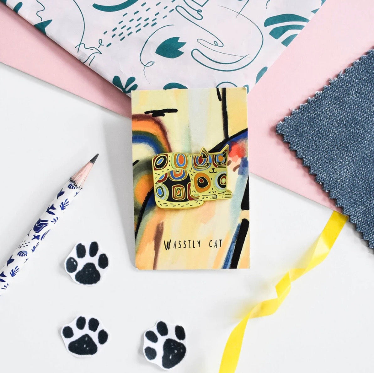 Colourful cat-shaped pin on backing card with abstract design, on a table with craft supplies.