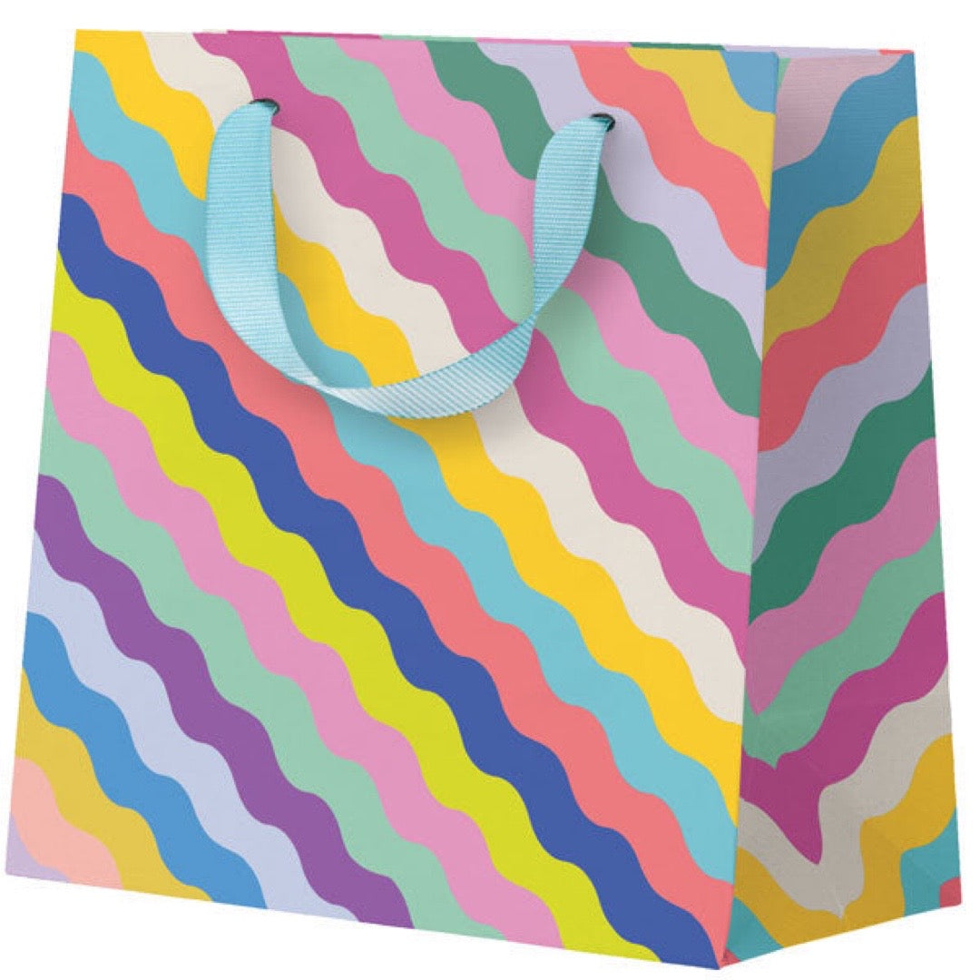 Colourful wavy patterned gift bag with blue handles on a white background.