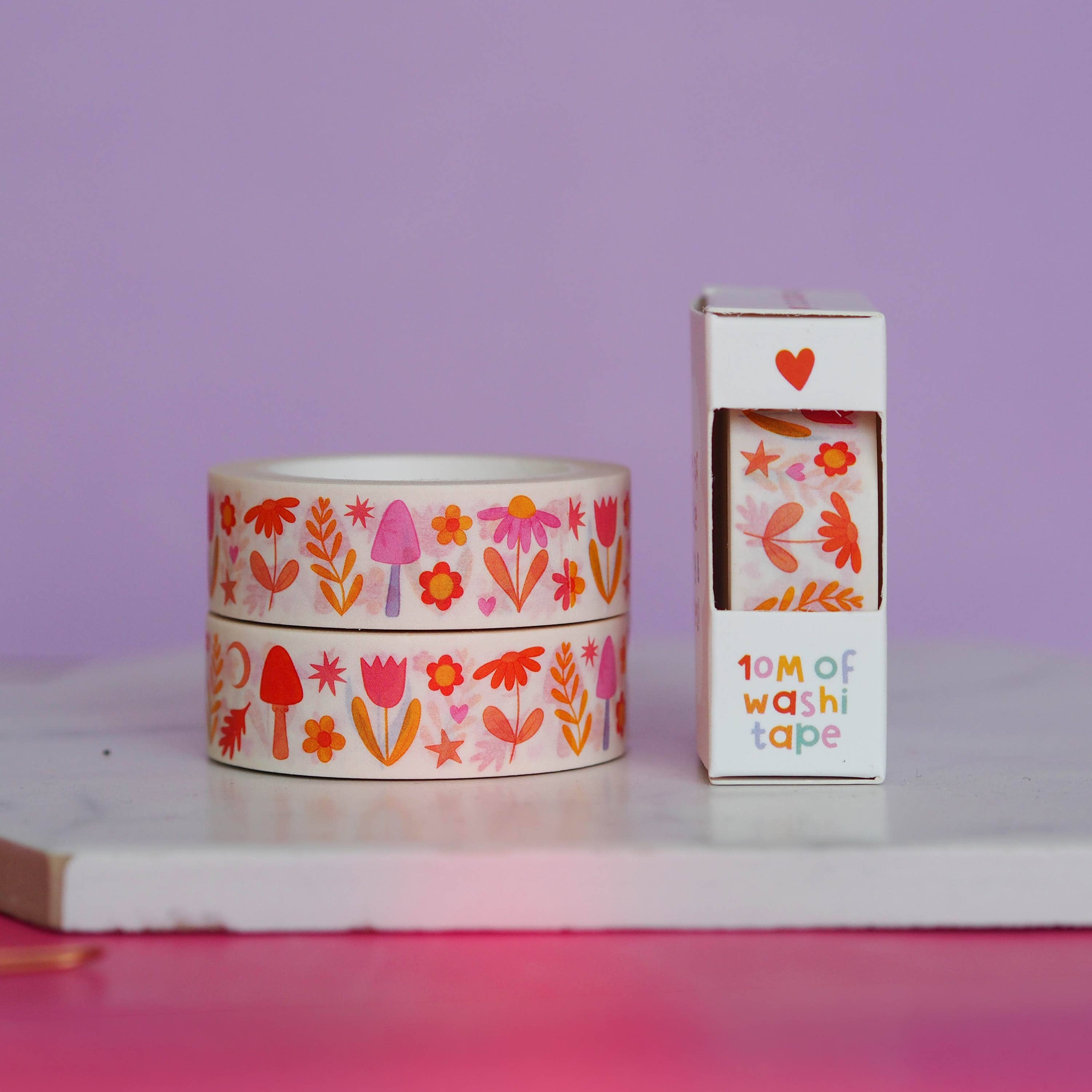 Two rolls of floral-patterned washi tape with a box on a white surface against a purple background.