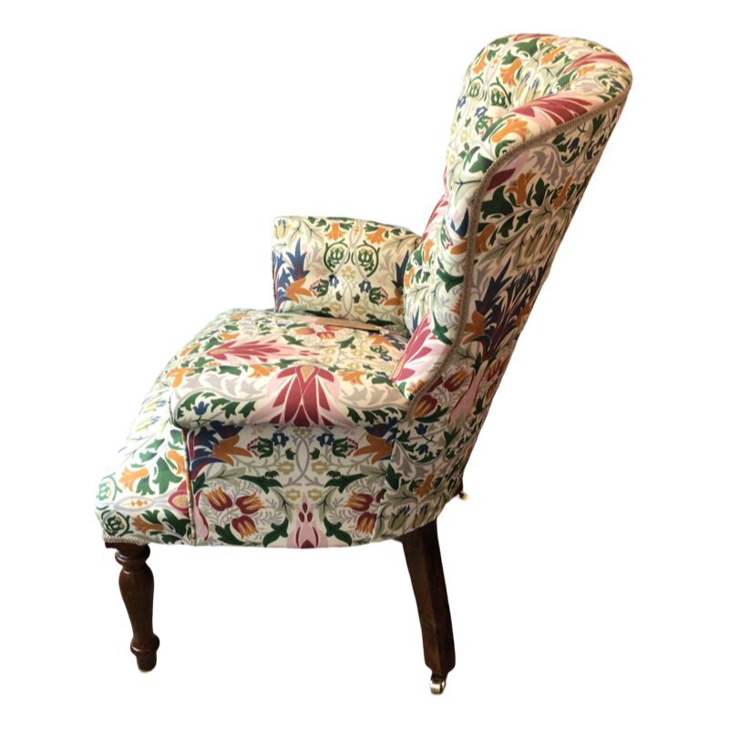 A hand-crafted occasional armchair in cream linen fabric with a multicoloured floral William Morris inspired design, featuring mahogany legs and gold castors.