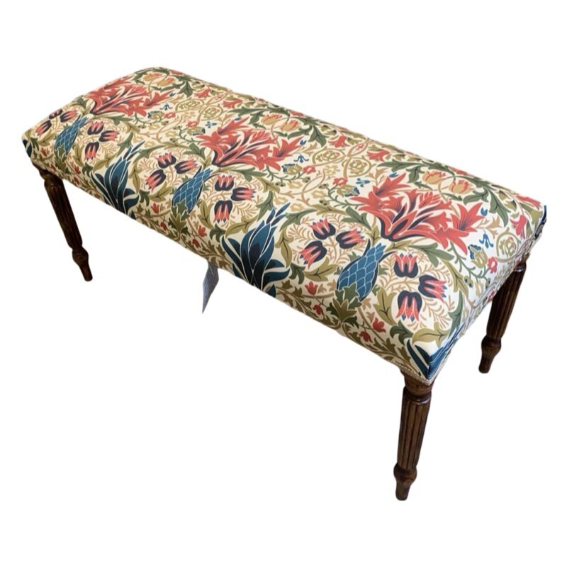 A rectangular bench covered in cream linen fabric with a multicoloured floral William Morris style design, featuring mahogany legs and cream binding.