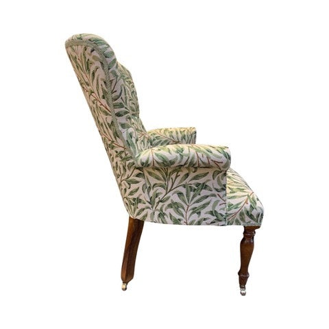 A William Morris style armchair with green leaf pattern on fabric, button-back design, and mahogany stained legs.