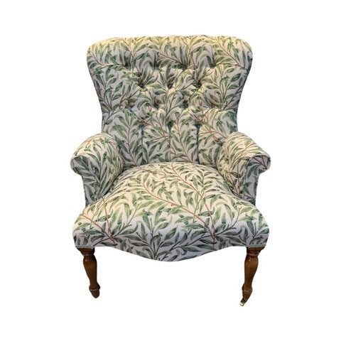 A William Morris style armchair with green leaf pattern on fabric, button-back design, and mahogany stained legs.