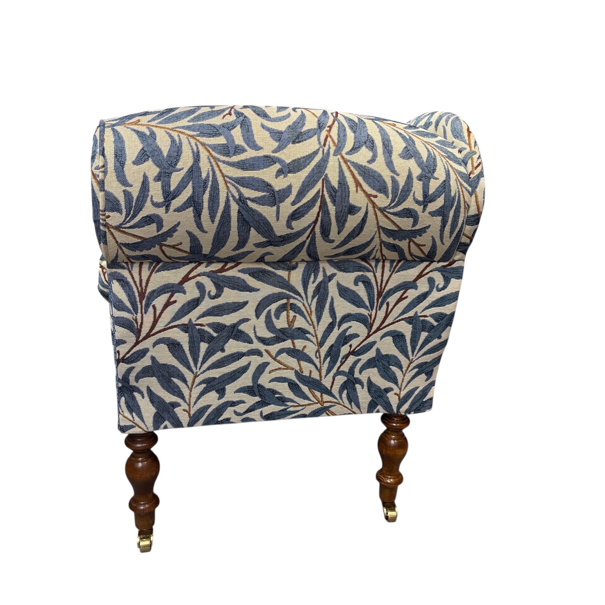 A handcrafted occasional chaise lounge in fabulous woven William Morris It is covered in beautiful William Morris Willow Bough tapestry-style fabric in navy blue and cream. It is finished with navy blue binding and has mahogany-stained wooden legs. The chaise lounge also comes with a removable bolster cushion and brass coloured castors.