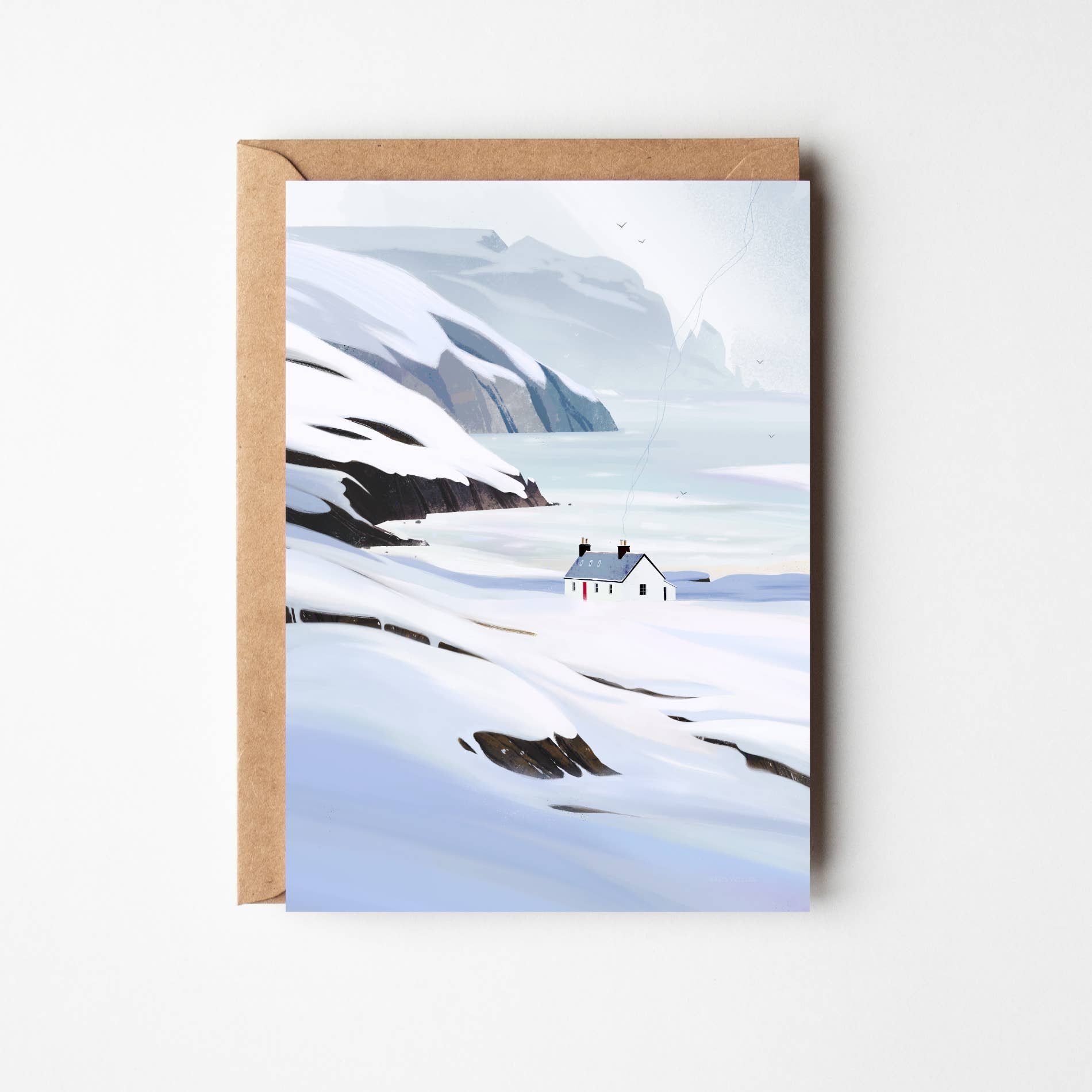 A square greeting card with a brown kraft envelope, featuring a minimalist winter landscape illustration of snow-covered mountains, a small white cottage, and pale blue water under a soft light sky.