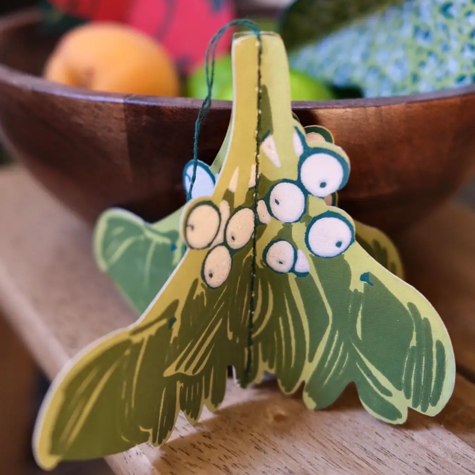 A paper fold-out Christmas decorations of mistletoesitting on a wooden shelf.