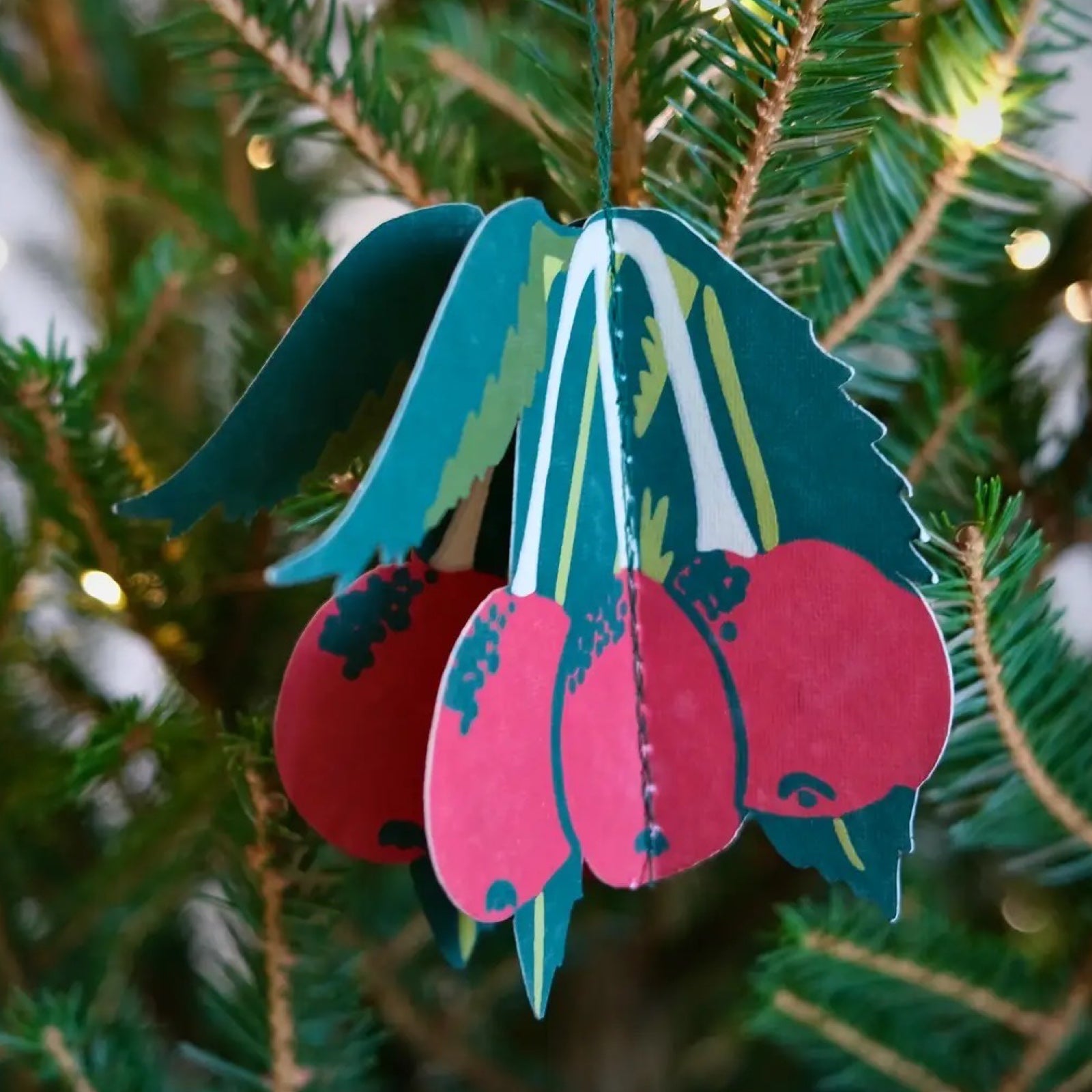 A paper fold-out Christmas decorations of red berries hanging on a Christmas tree.