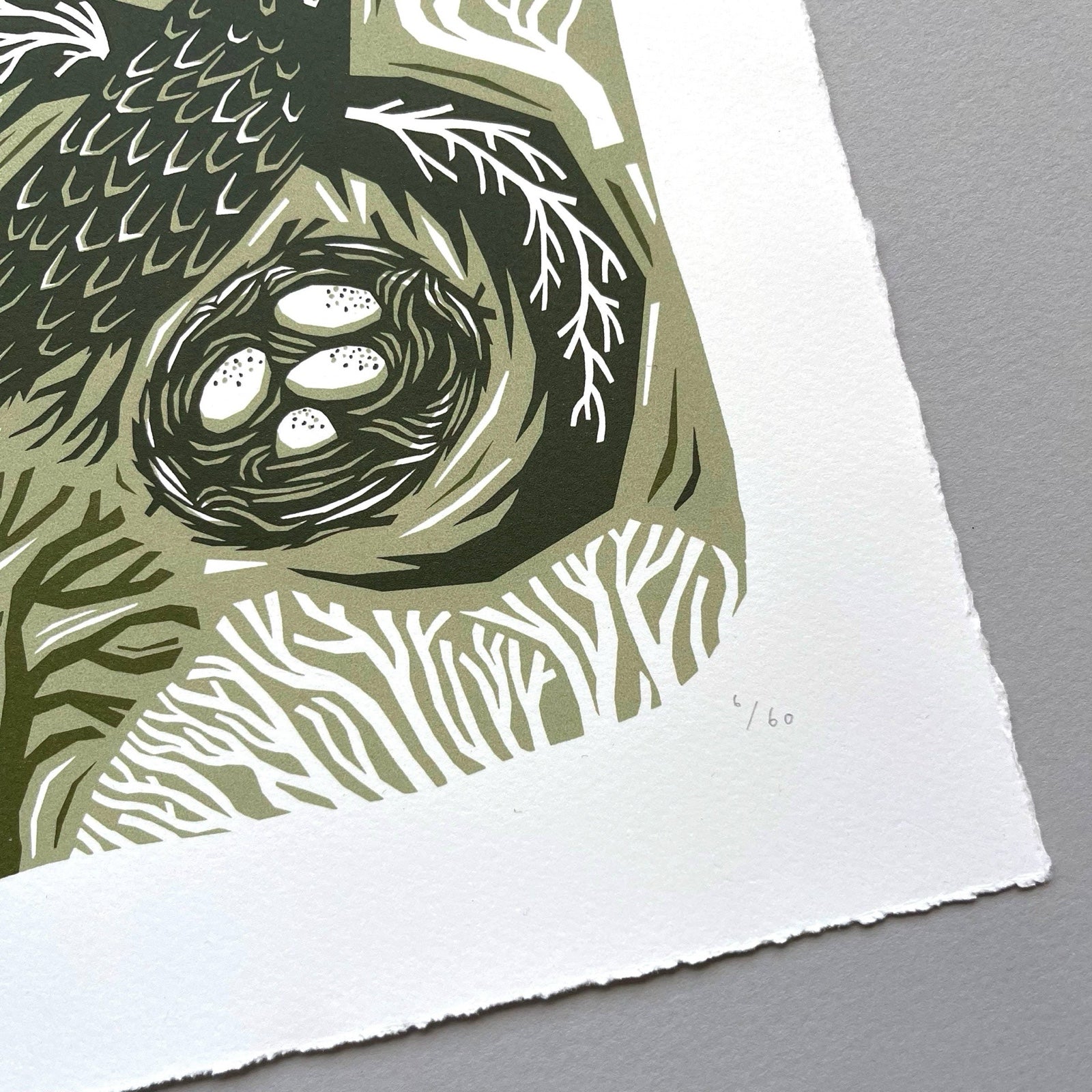 This woodland bird screen print is printed in three shades of green. It features a bird flying over its nest with trees behind, and is printed on hand-torn, thick, satin white paper.