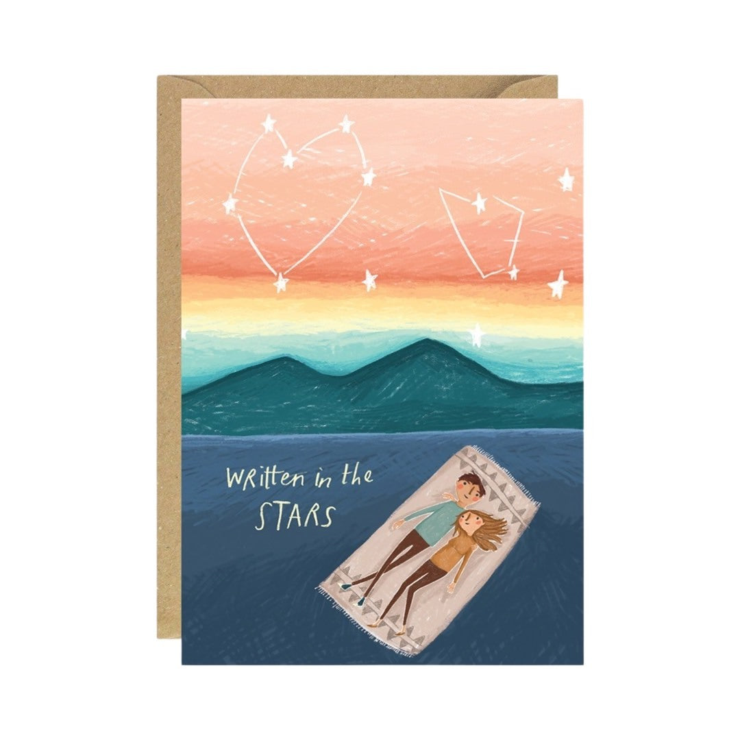 Love and friendship card featuring a couple lying on a blanket staring up at the sky where the stars have formed two love hearts, with the text 'Written in the Stars'.