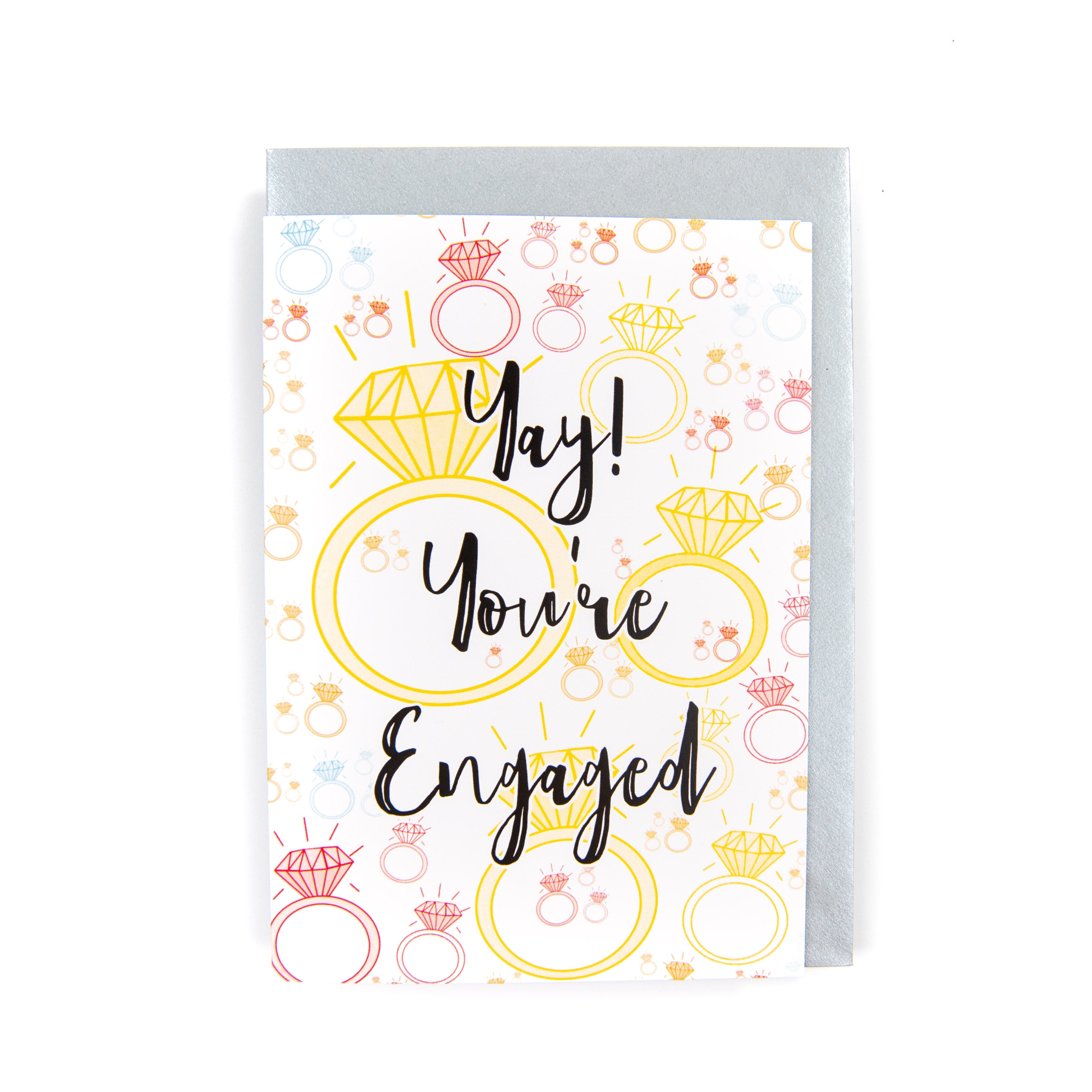 A greeting card with a colorful design, reading 'YAY! You're Engaged' with a diamond ring illustration and small ring-themed graphics.